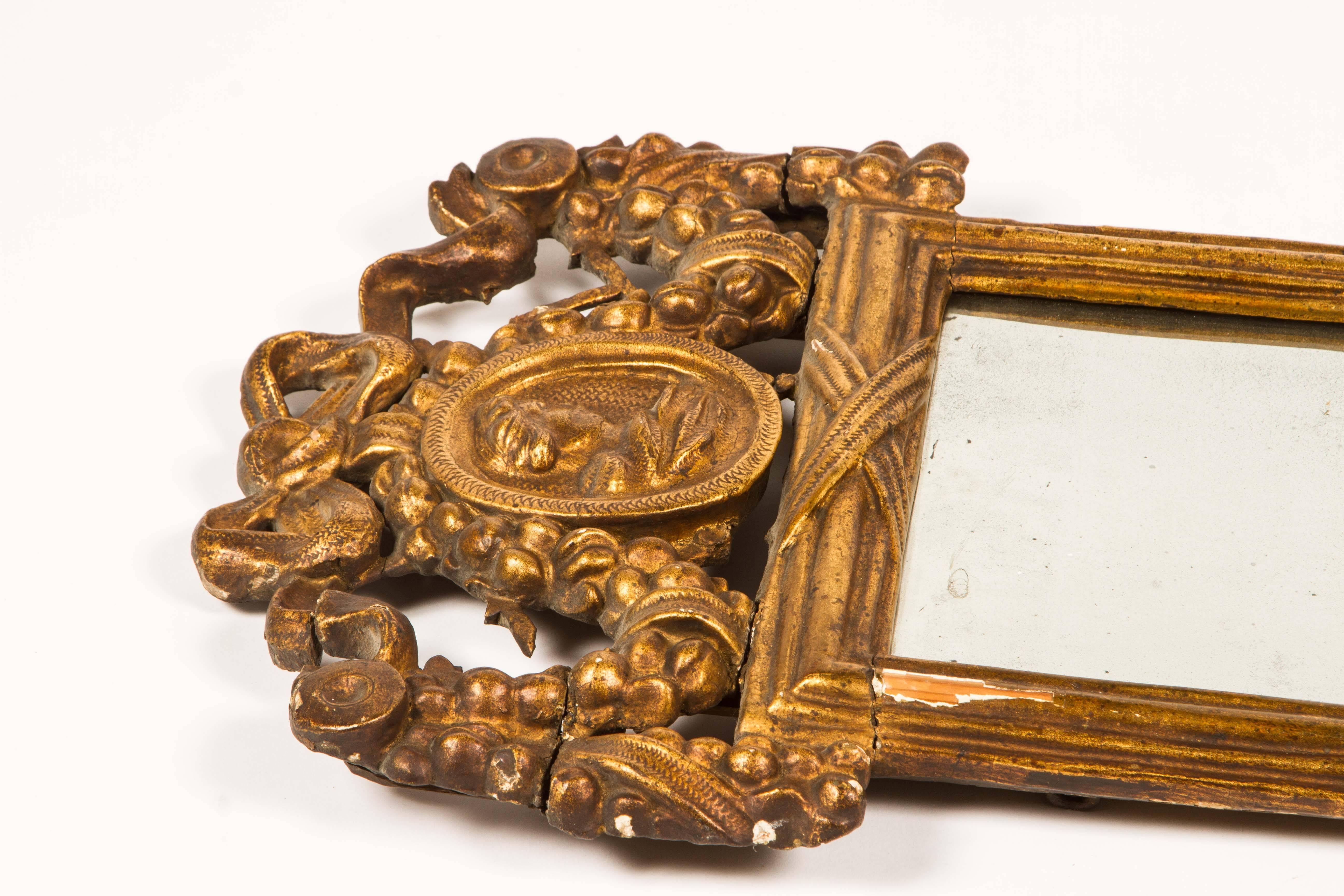 18th century Louis XVI style giltwood mirror with hand-carved embellishments featuring a portrait medallion at the pediment, and swags of ribbon and garland on the top and bottom.