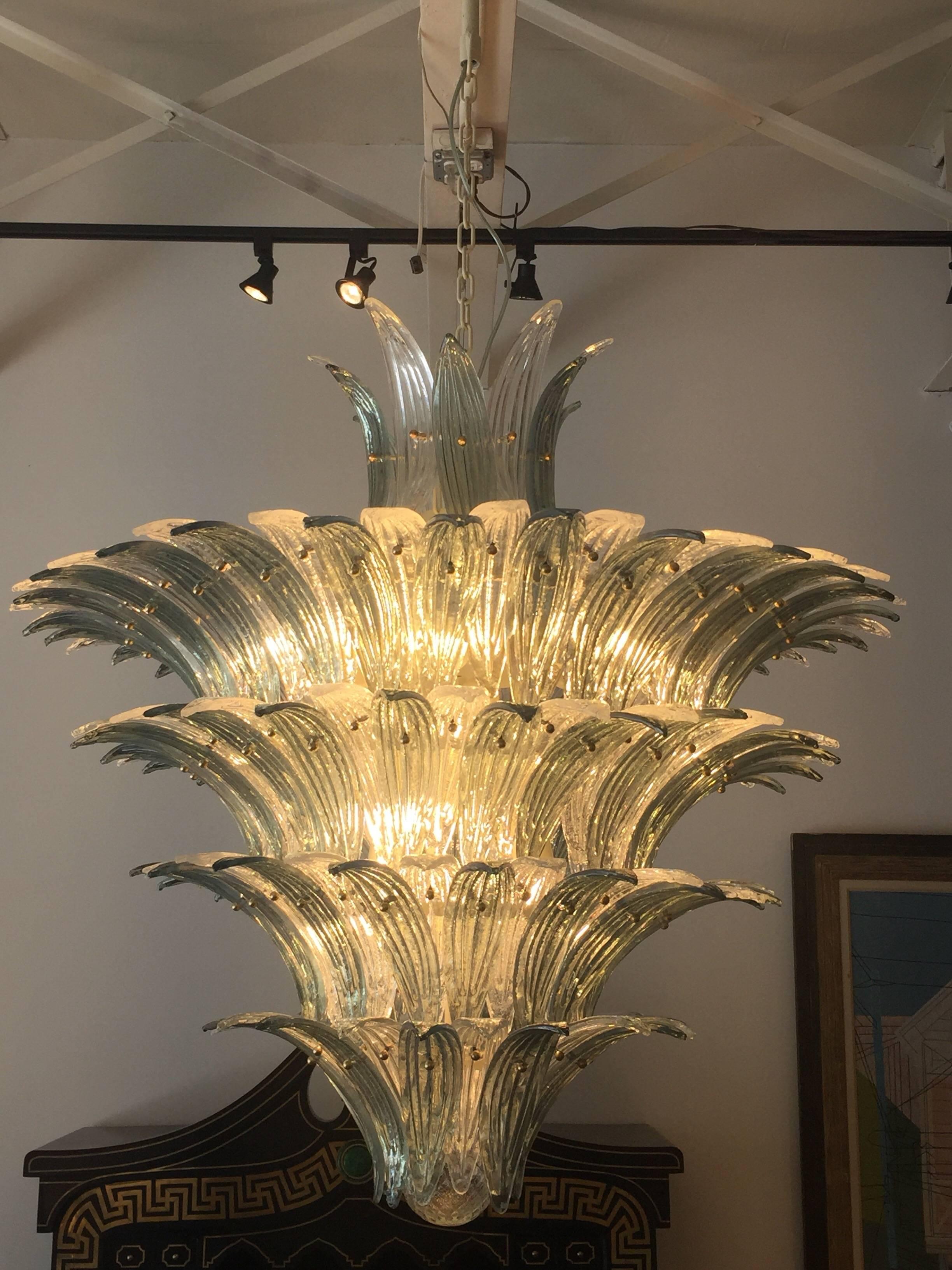 Often attributed to Marius-Ernest Sabino, these new production large-scale chandeliers (four tiers) are interlaced glass palm fronds in clear and grey/blue iridescent tones. We have two identical fixtures if your project requires - sold