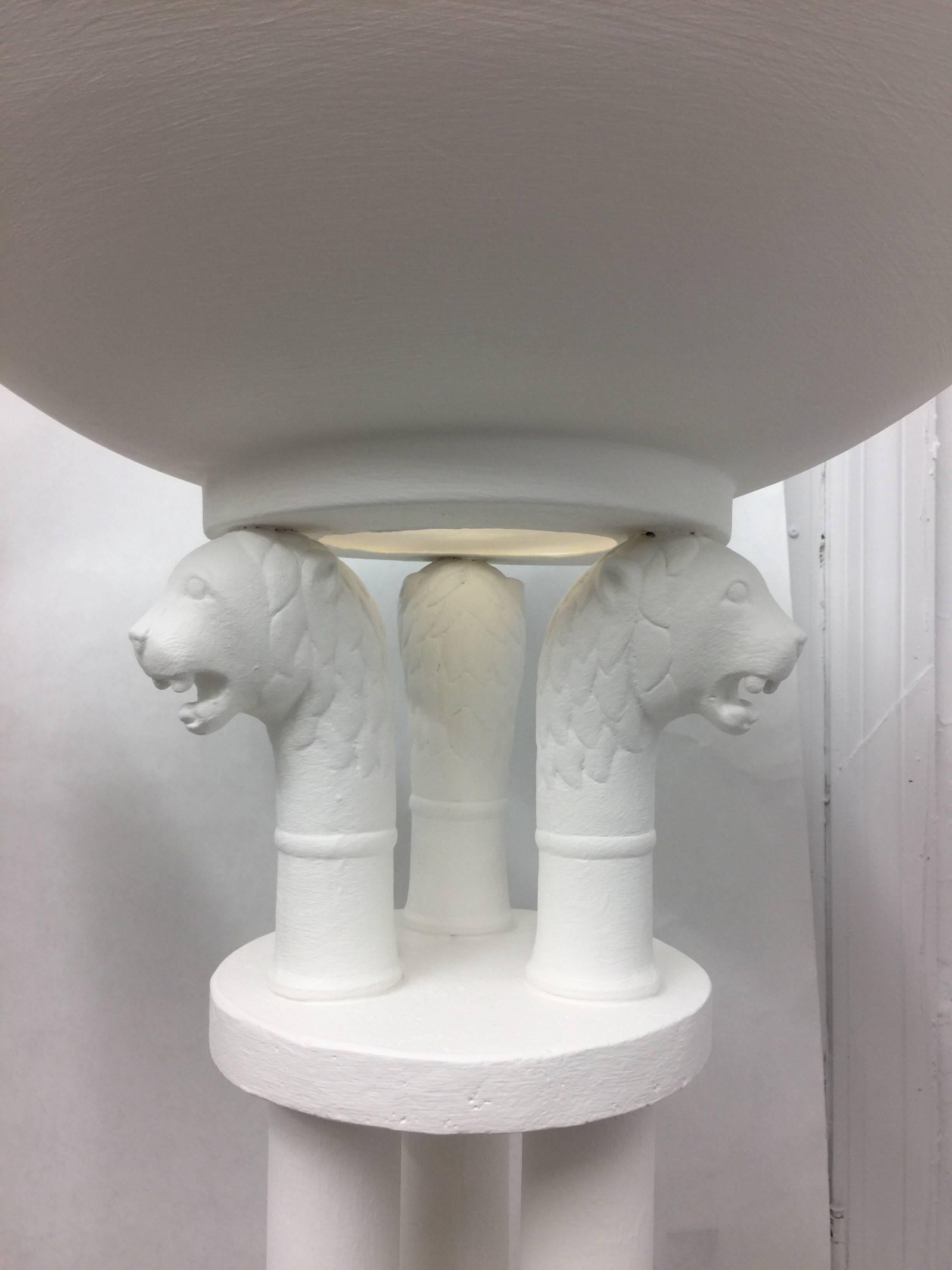 Topped with three Roman style lion heads and an oversized saucer diffuser for up-lighting, these matching pair of floor lamps are finished in a soft plaster tone. Whimsical and very much in the manner of John Dickinson.