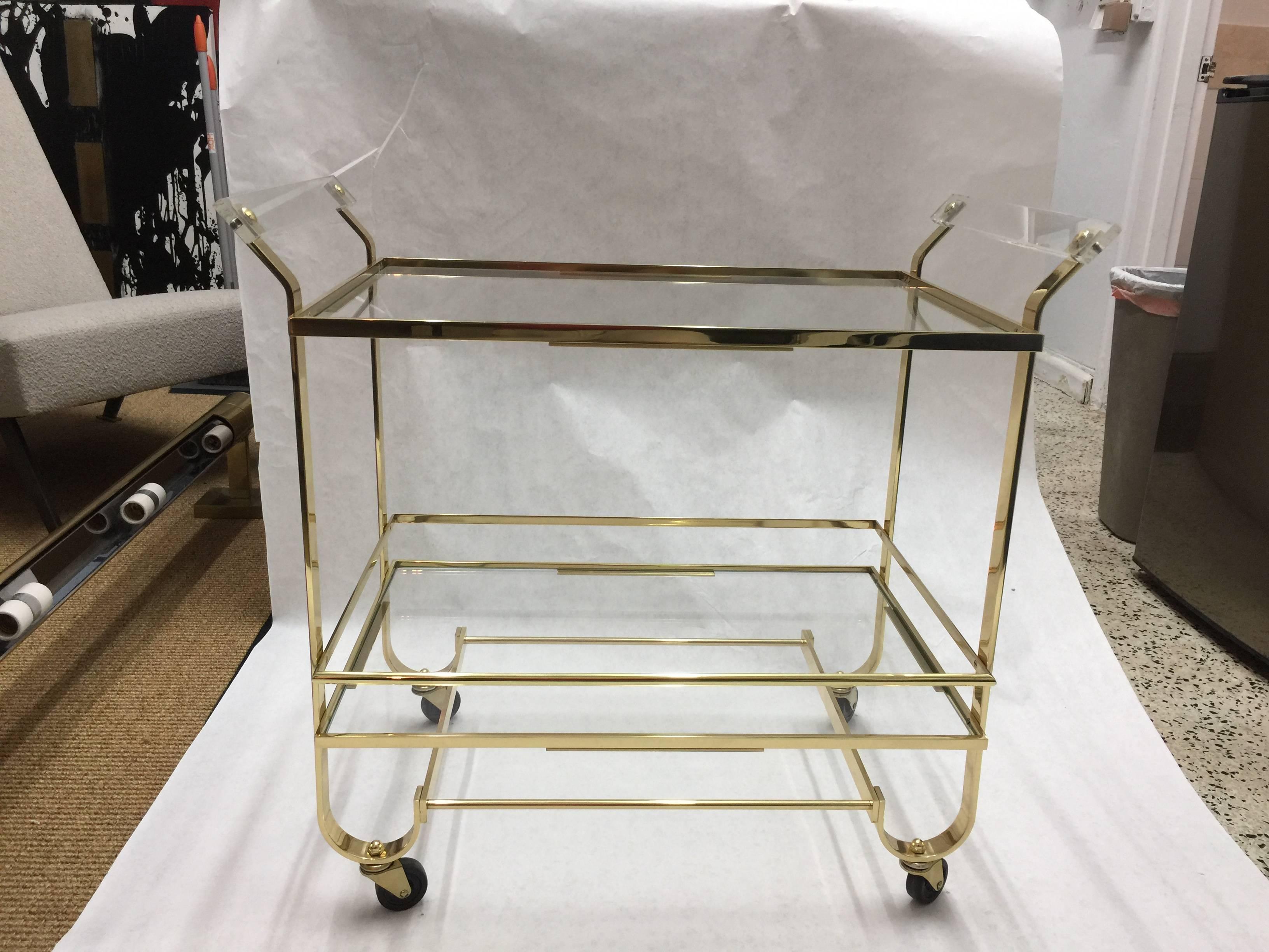 Original vintage Lucite handles and polished brass bar cart. Two-tiers of glass shelves this cart is on casters for easy rolling.