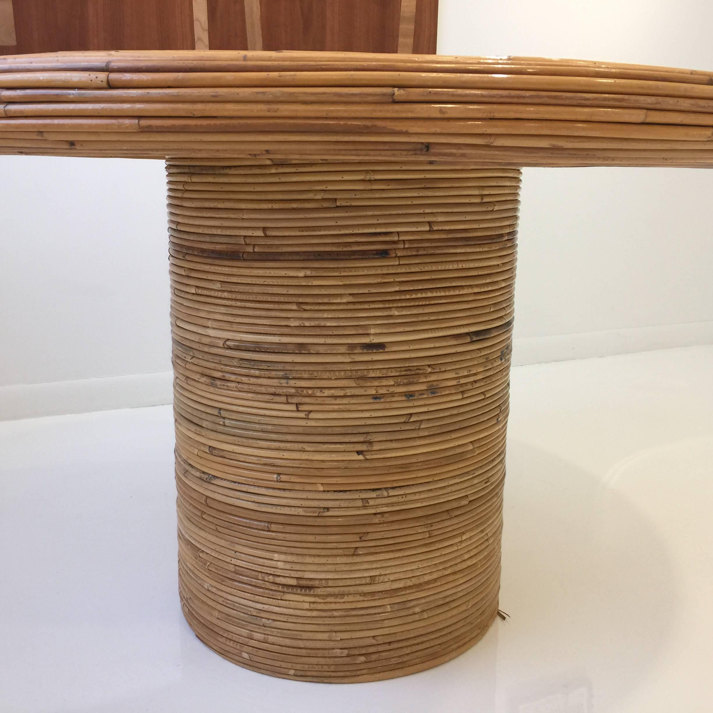 A unique rattan dining table by Henry Olko for Willow and Reed, signed and dated 1978. Black glass sits atop a thick cylindrical base.