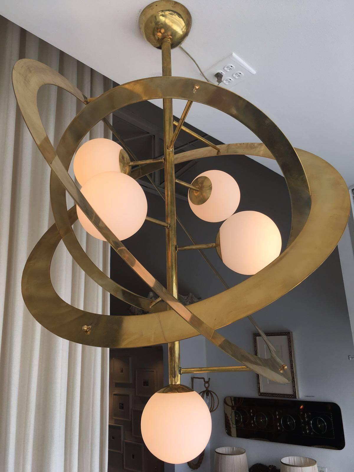 This five-light frosted globe chandelier is crowned by three large brass rings reminiscent of a futuristic planet.