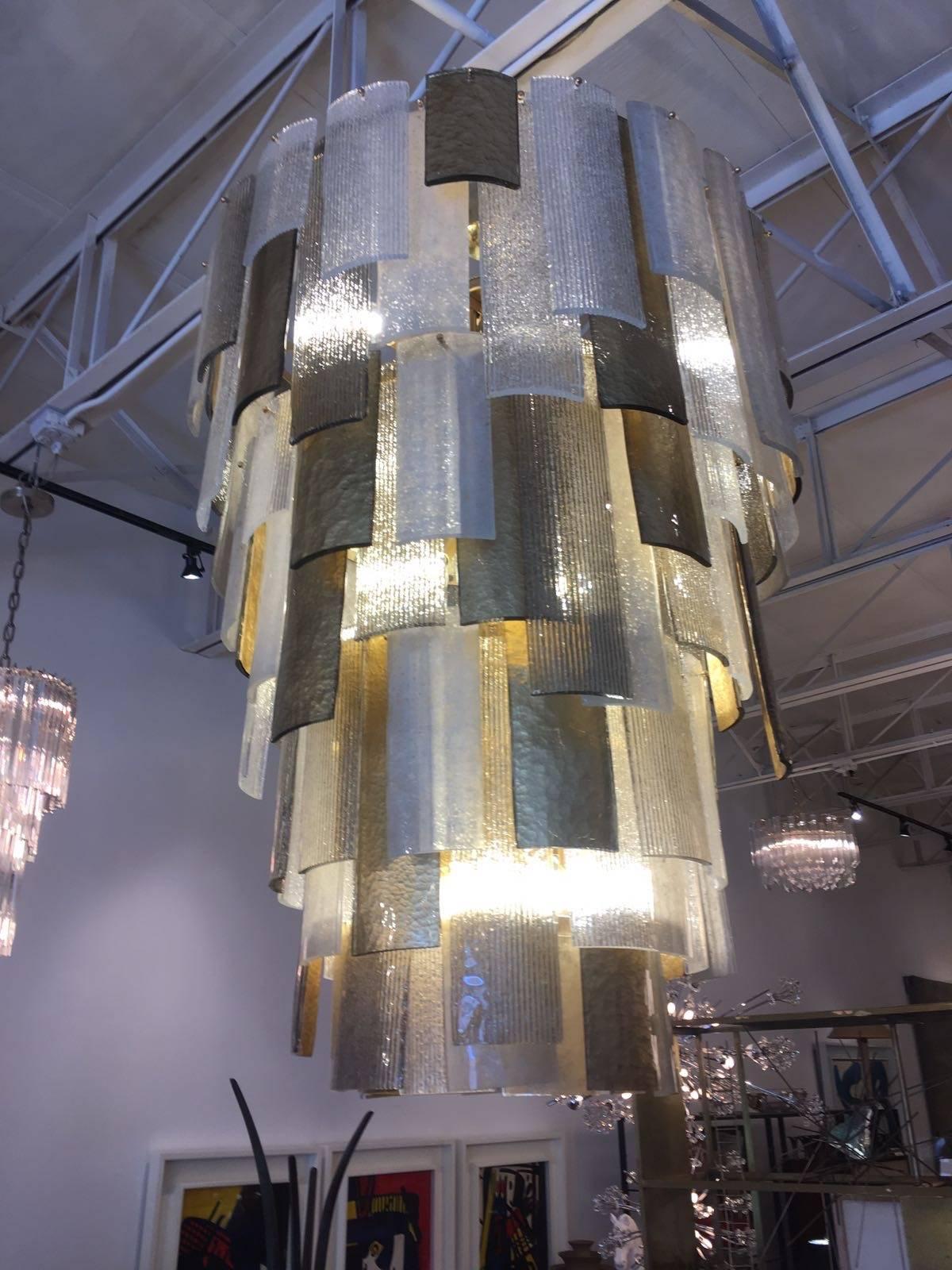 Murano glass chandelier with four cascading levels of layered Murano alternating textured glass and gold leaf glass, on a steel structure with brass fittings. This spectacular chandelier holds nine medium base lights and has been rewired for the
