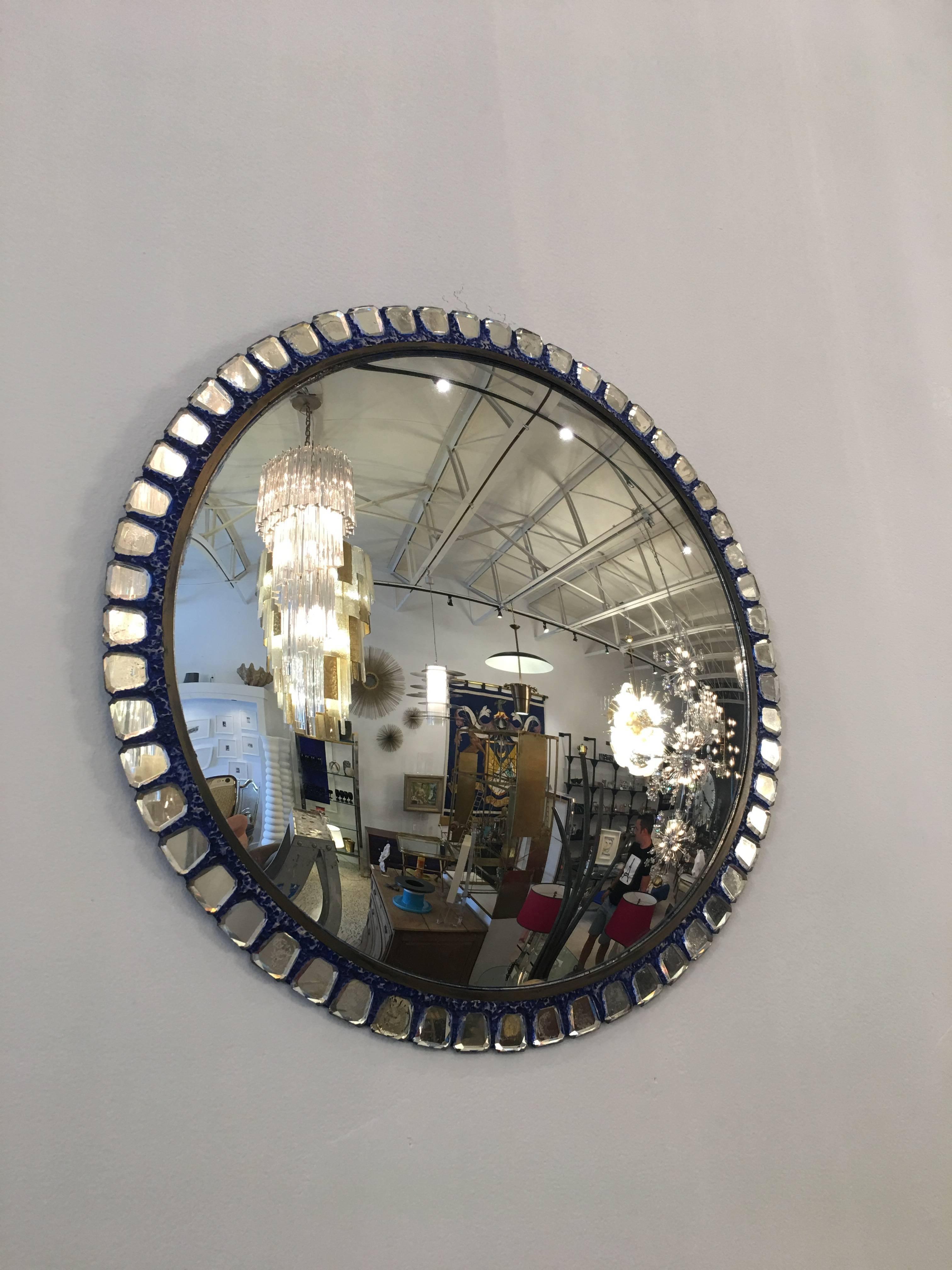 Exquisite details throughout small faceted mirrors surround this convex wall-mounted mirror. A subtle Yves Klein blue tint to plaster mold surround. Brass trim surround makes this a solid and important Vautrine style treasure.