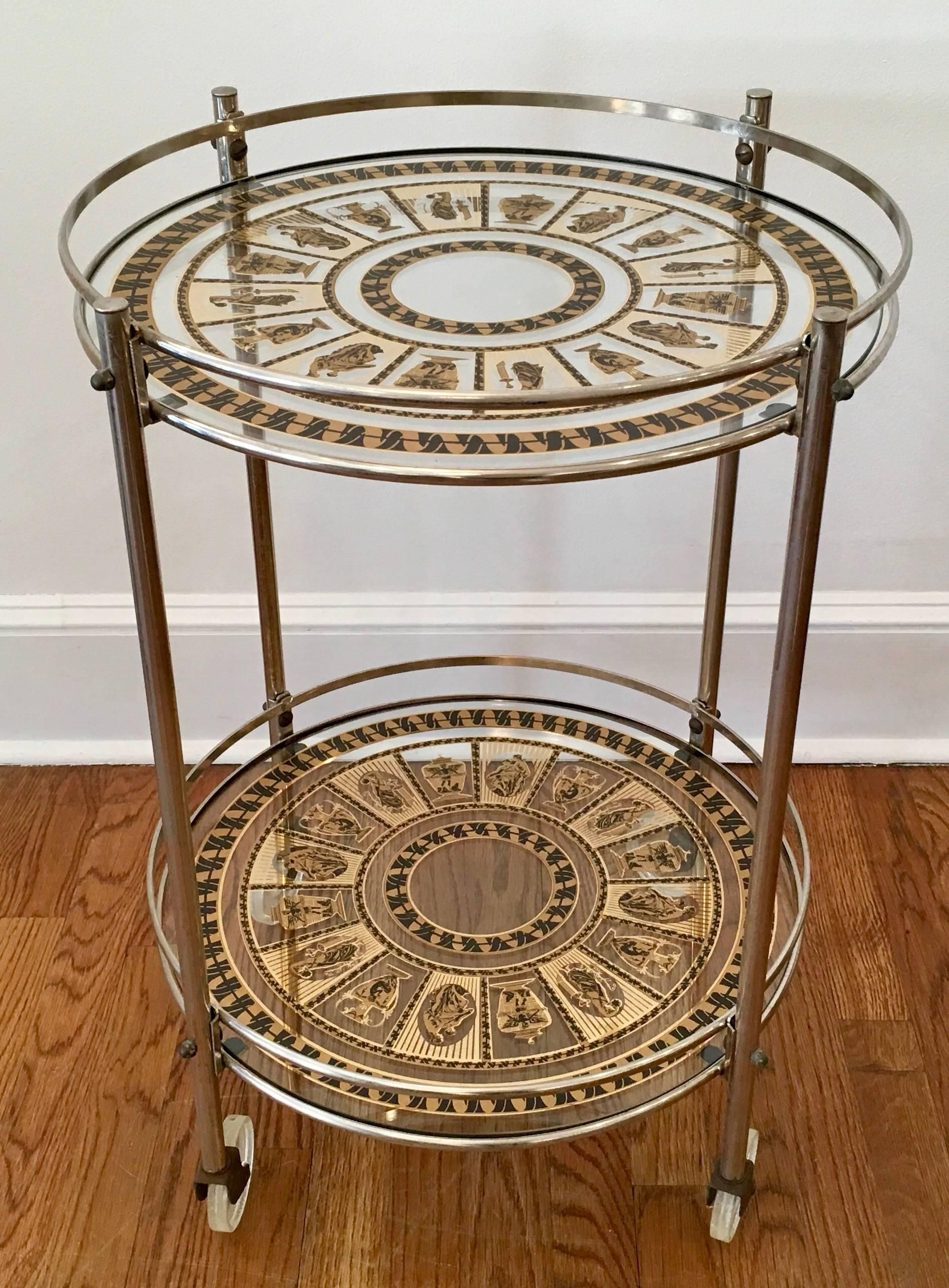Delightful two-tiered bar or serving cart. The cart has stencilled black and gold alternating images of Greek vessels and Greek figures painted on glass. Chrome and glass cart has great appeal.