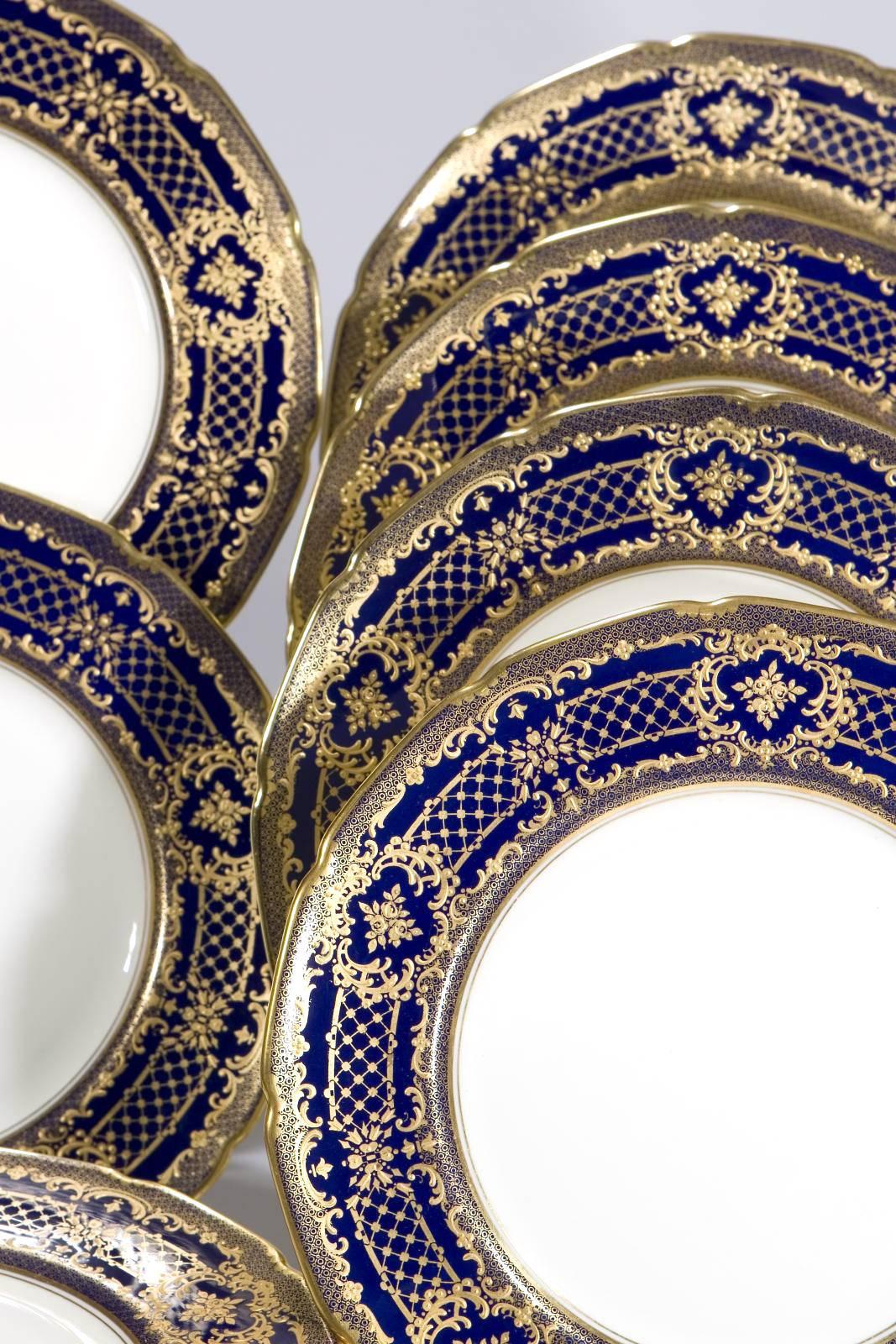 A set of 16 Royal Doulton cobalt blue border dinner plates with exquisite raised paste gold roses, embellishing the deep cobalt borders. Extremely versatile as both service/presentation plates as well as dinner plates with subtle, barely ivory