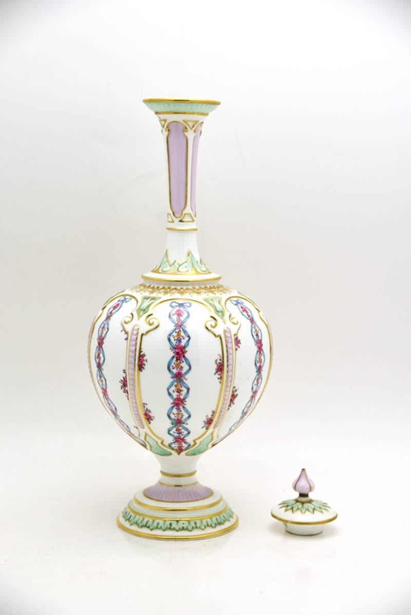 This vase, made by Royal Worcester, is decorated in an unusual Art Nouveau style incorporating a beautiful combination of soft and vibrant colors. The shape is tall and elegant and finished with a matching lid with finial. A white ground body is