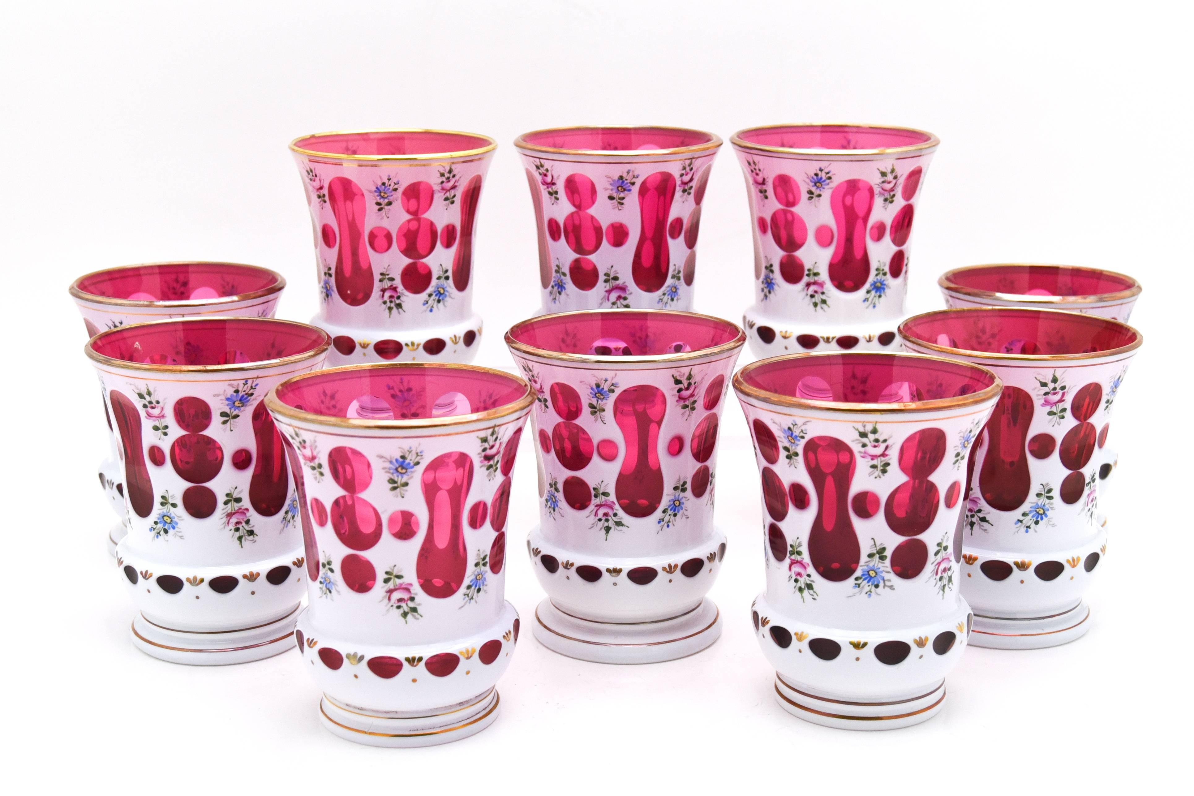 This is a very versatile set of ten Bohemian tumblers with wonderful enamel decoration. Each one is hand blown cranberry crystal with white overlay, cut to cranberry and then hand-painted with polychrome enamel flowers, all trimmed in gold. Not only