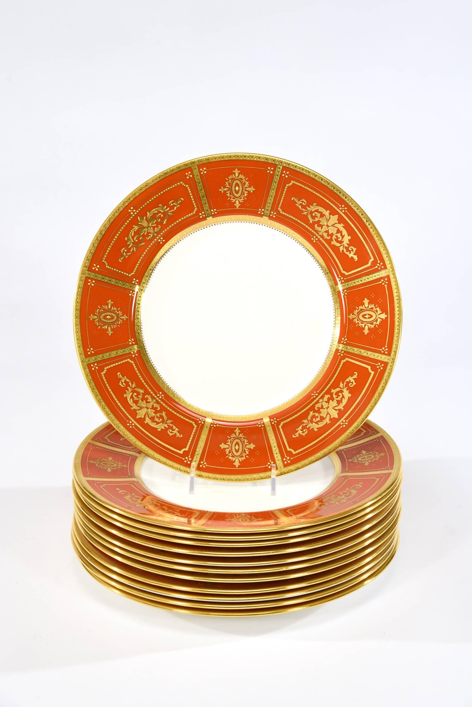 This is a gorgeous set of 12 Mintons dinner plates with bittersweet orange borders which are decorated with raised paste gold in a neoclassical motif and trimmed with an acid-etched gold border. A rare color, these dinner or service plates exemplify