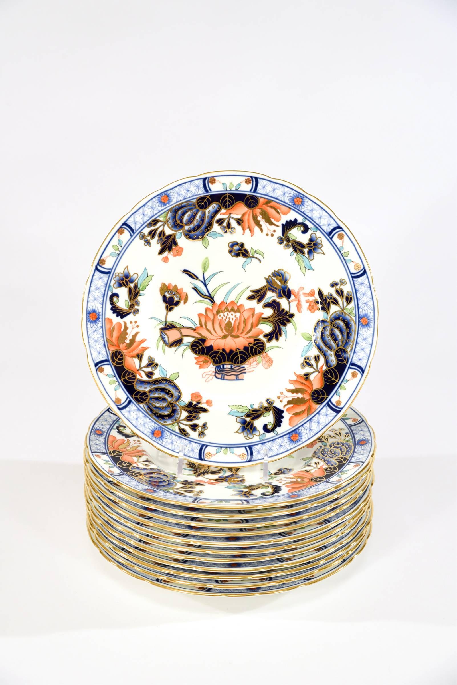 The polychrome enamel Japonesque motif, using the Imari palette decorates these 12 pristine dessert plates made by Royal Crown Derby. The combination of soft blue, cobalt blue, bittersweet orange and green all trimmed and highlighted in gold makes