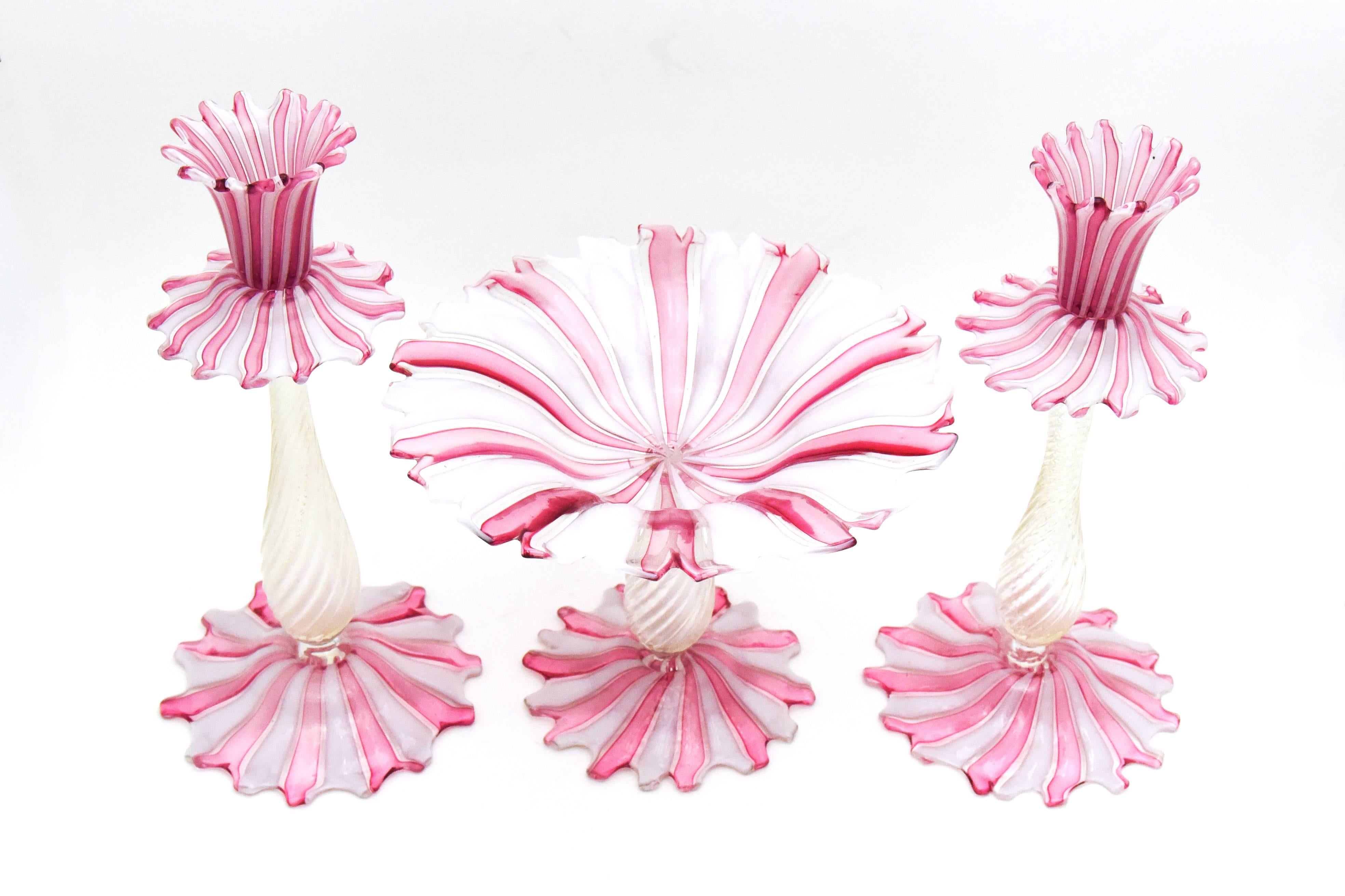 I call this set peppermint candy! This is an unusual design and technique of Venetian glass incorporating the ever popular pink and white stripes with clear optic swirl stems, subtly infused with gold leaf. The feet and bobeches have the added