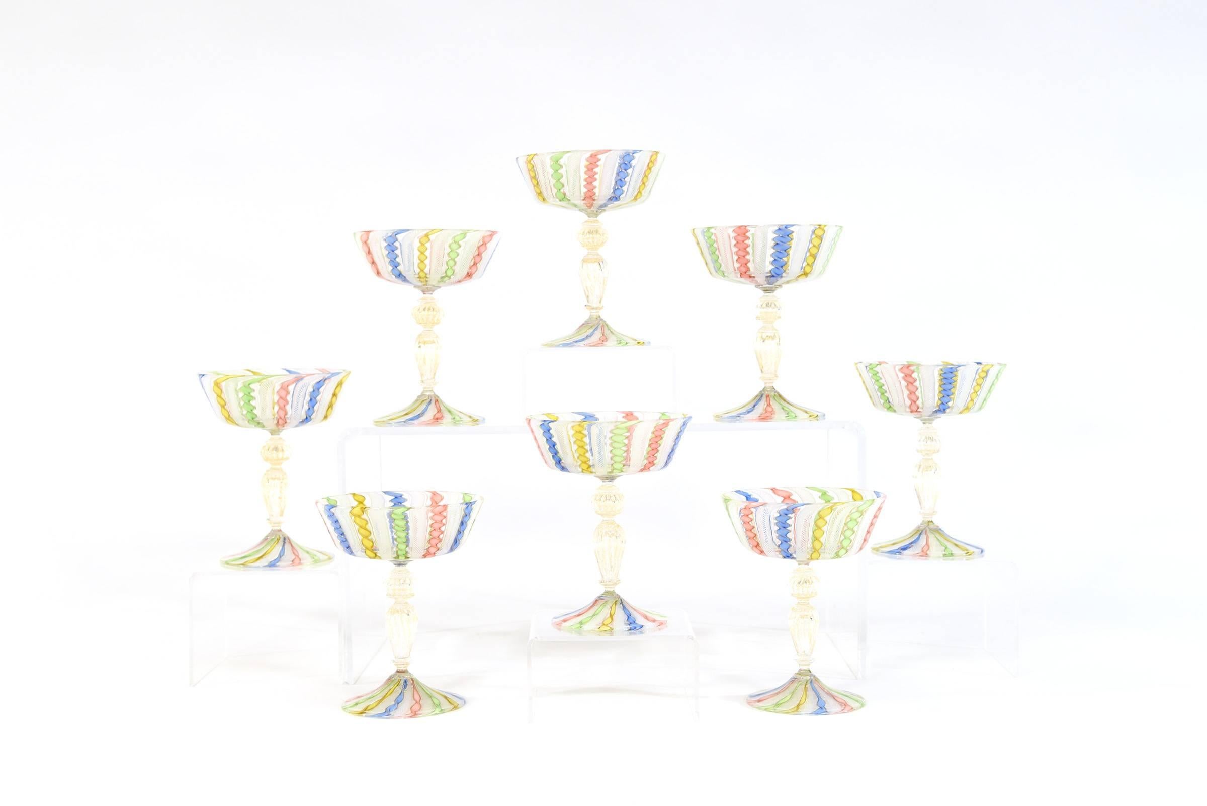 This set of eight champagne goblets was made in Murano and exhibit the master glassblowing techniques of Salviati. The alternating multicolor and gold canes of latticcino encircle the bowl and foot with a gold leaf infused stem, which creates an