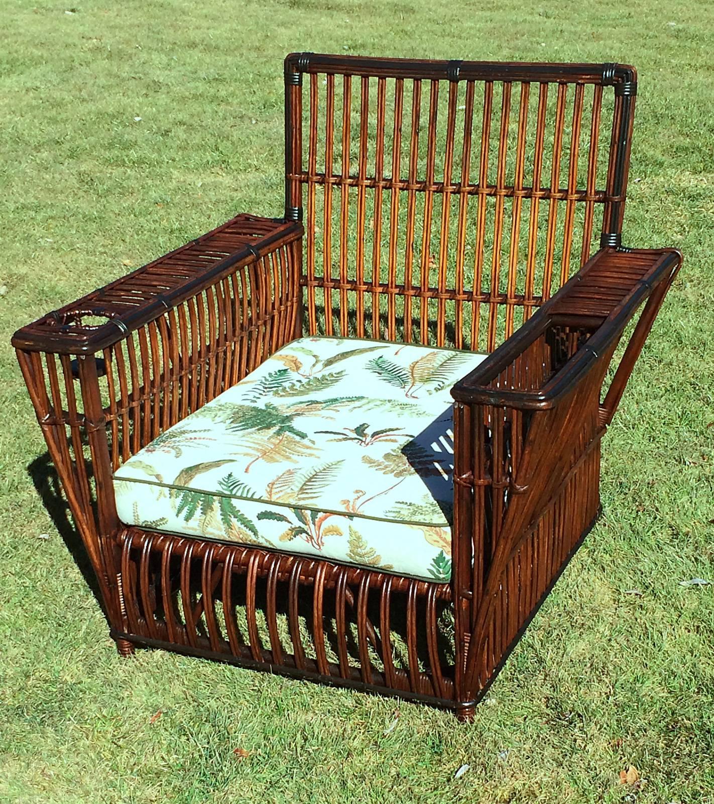Large-scale Stick Wicker armchair in natural stained finish with black trim. Magazine holder in left arm, & beverage holder in right arm. Closely paired reeds overall. Seat platform of paired reeds having older cushion & back pillow. Celluloid label
