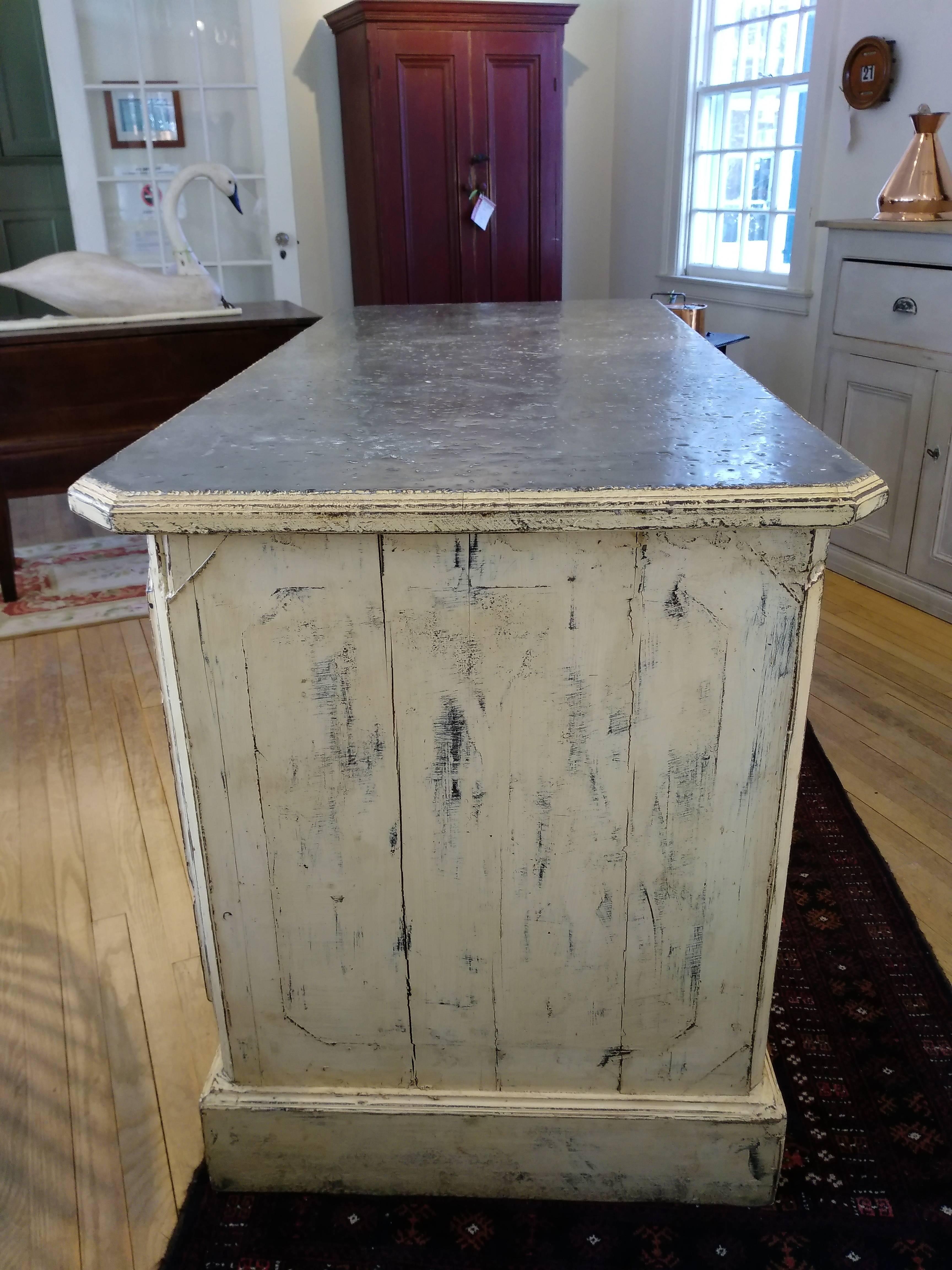 This piece came from a bakery store in the south of France. The piece is totally original, including the zinc top, hardware and shelves. It has been repainted by our dealer, a soft butter color. The counter is finished on all sides and has a door