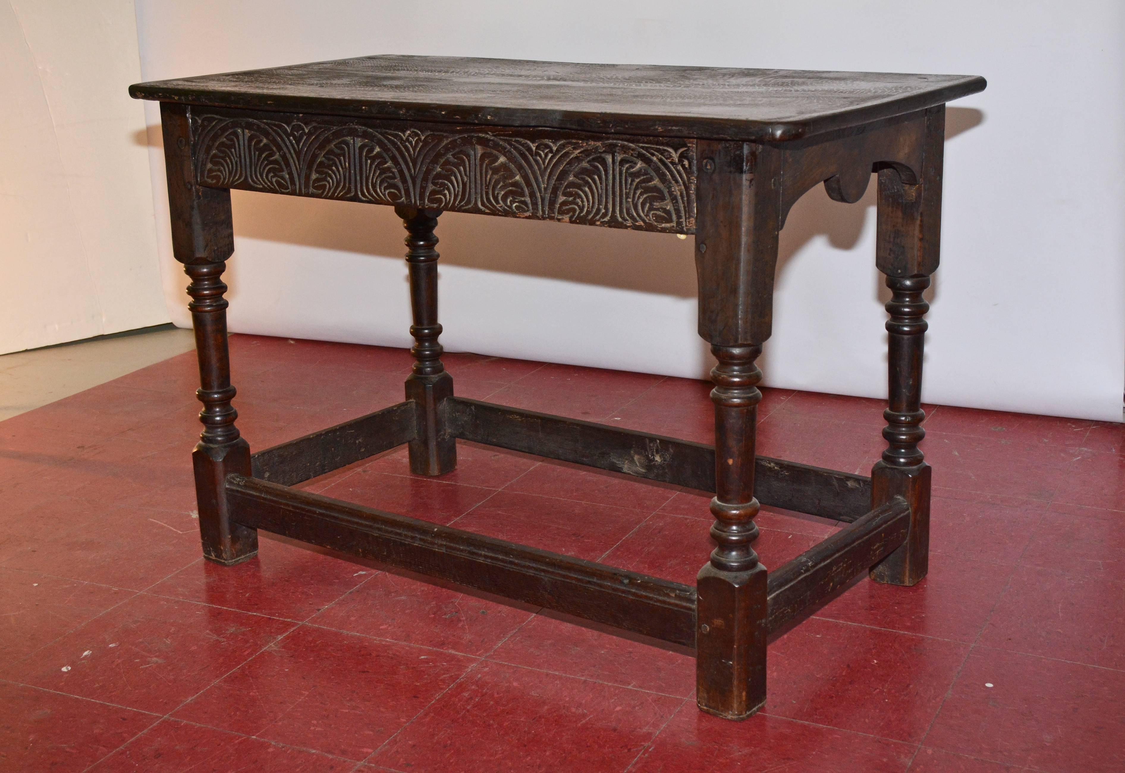 This English library or sofa table has aprons of stylized leaves carved within repeated half circles, turned legs and stretchers.