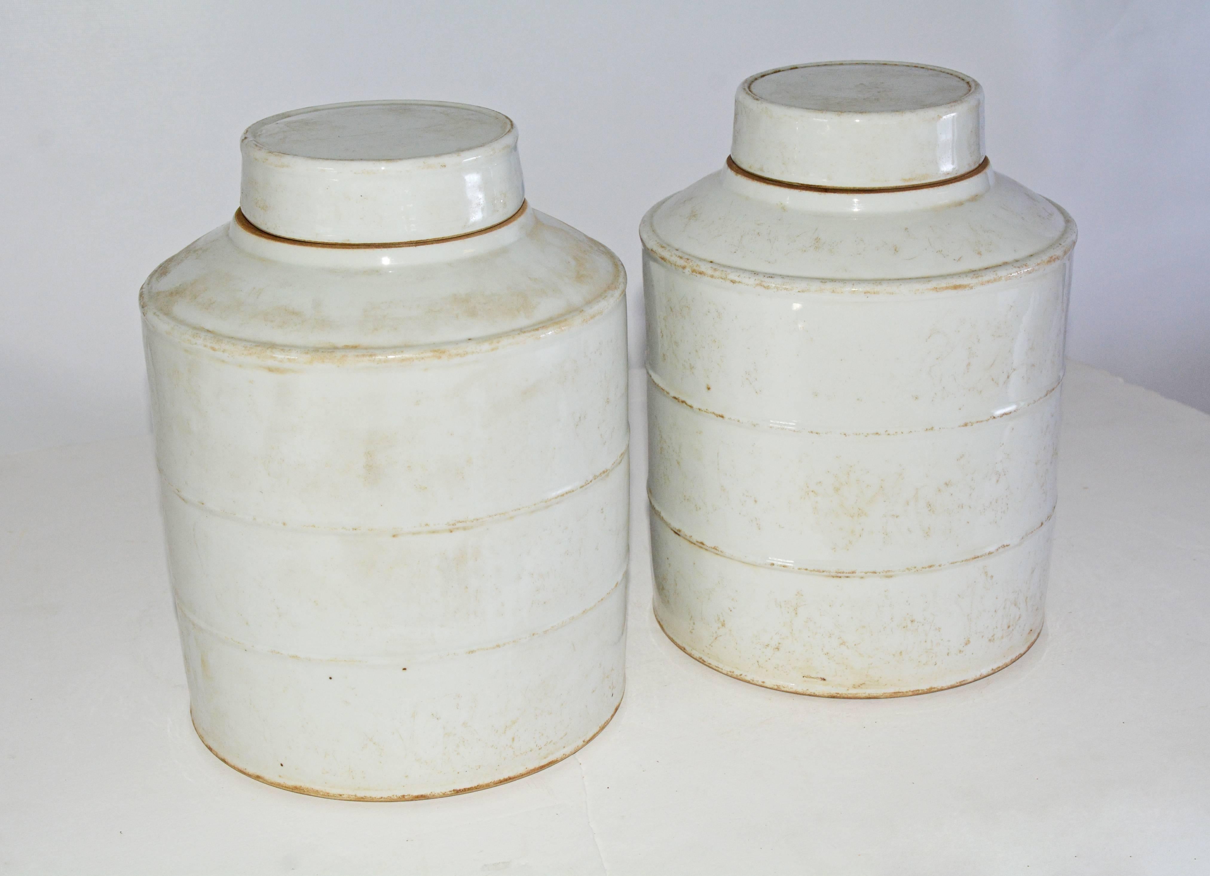 The pair of white vintage Chinese ginger jars and lids are made of pottery. The sides are divided into three sections by raised bands.