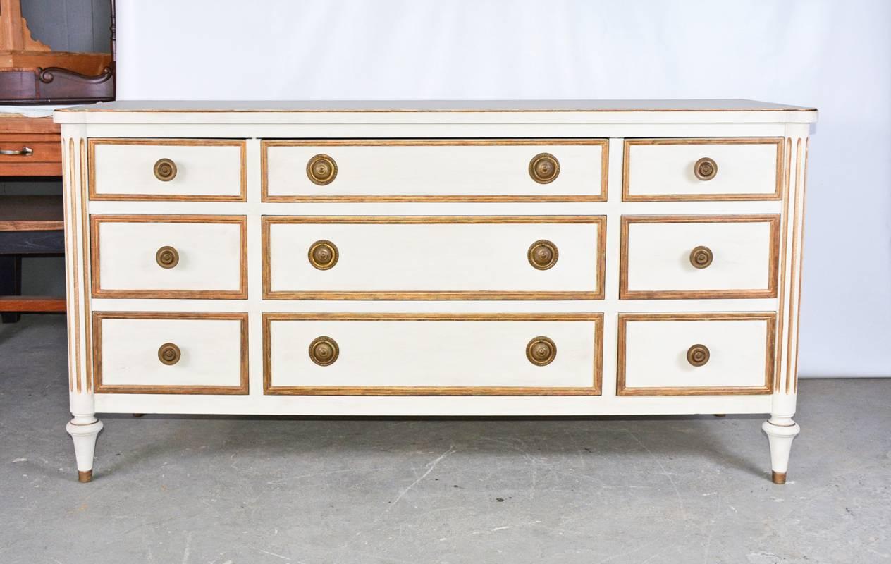 The white vintage neoclassical dresser has gilt detailing and brass pulls. The nine drawers are all dovetailed. Label reads 