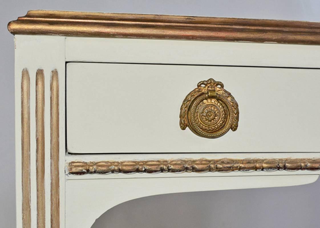 The vintage neoclassical dressing table, vanity, desk or night table has gilt detailing, fluted legs, brass pulls and curved stretchers. Drawers are dovetailed. Can be used as side table or nightstand. Label reads 