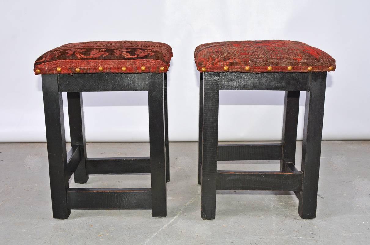 El par de taburetes contemporáneos recién tapizados con restos de alfombra antigua de oriente medio. Las patas de madera están pintadas de negro.