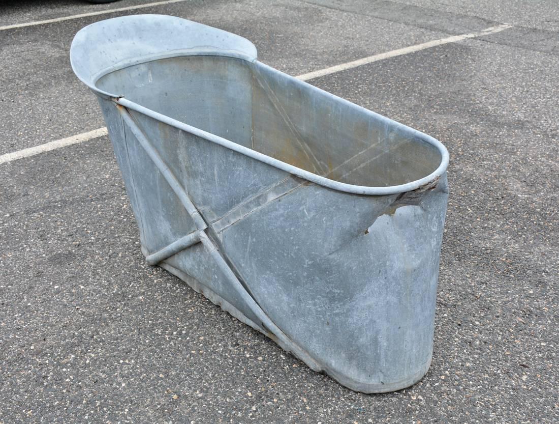 The antique 19th century French zinc bathtub with X-motif and a head rest and side braces to counteract the pressure of a tub full of water. There is an iron handle underneath the head rest. Wonderful as a planter.