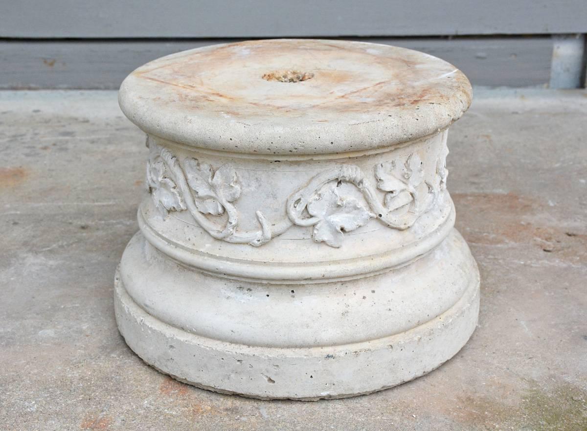 The round stone pedestal or low plinth is embellished with a band of ivy vines and leaves. Perfect for supporting potted plants in a garden.