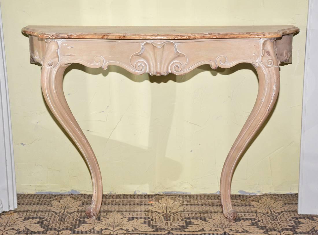 The antique hand-carved wood console or hall table is in the Venetian Rococo style. The color of the legs and frame is light brown and the top is painted faux marble in shades of brown and ocre yellow. There are holes in the back apron through which