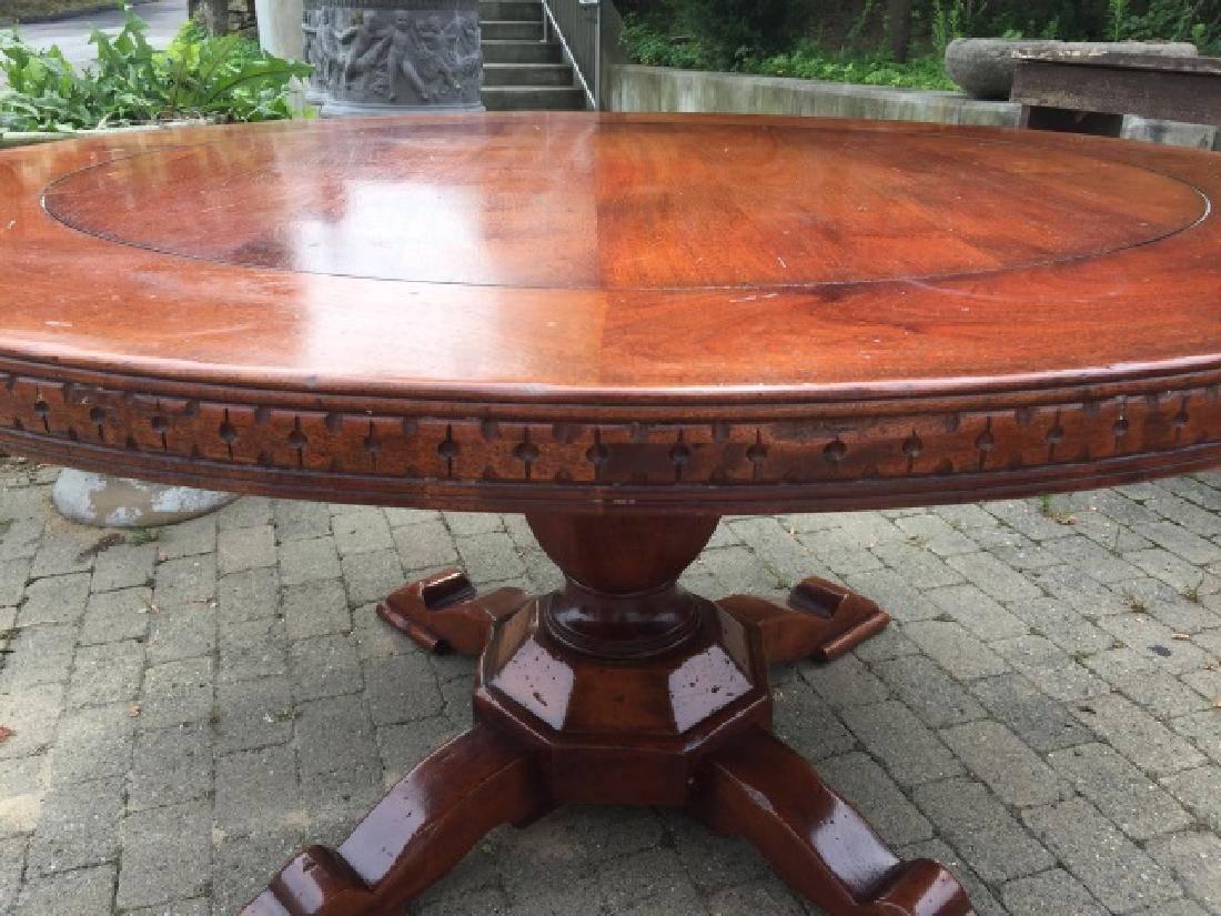 The vintage round mahogany dining or conference table with carved border has a centre pedestal base with four splayed feet. The pedestal is in the shape of an octagonal urn. The apron of the top has a repeat pattern of 