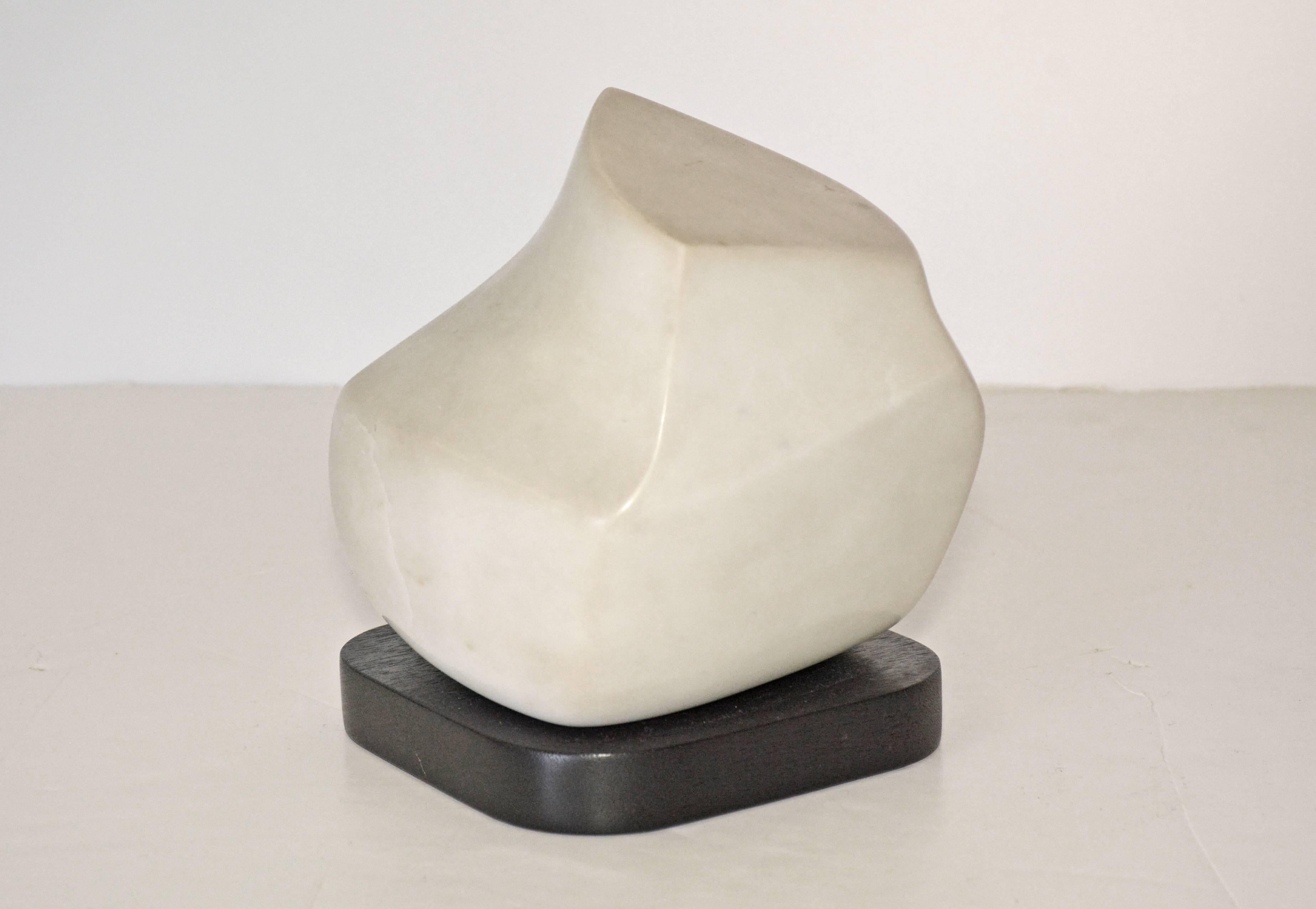 Small contemporary white marble sculpture sits on a black platform. Sculptor is Jean Downey (1931-2009). She was born in Canada, studied art in Illinois, New York and Connecticut. Her work is included in private and corporate collections in the US