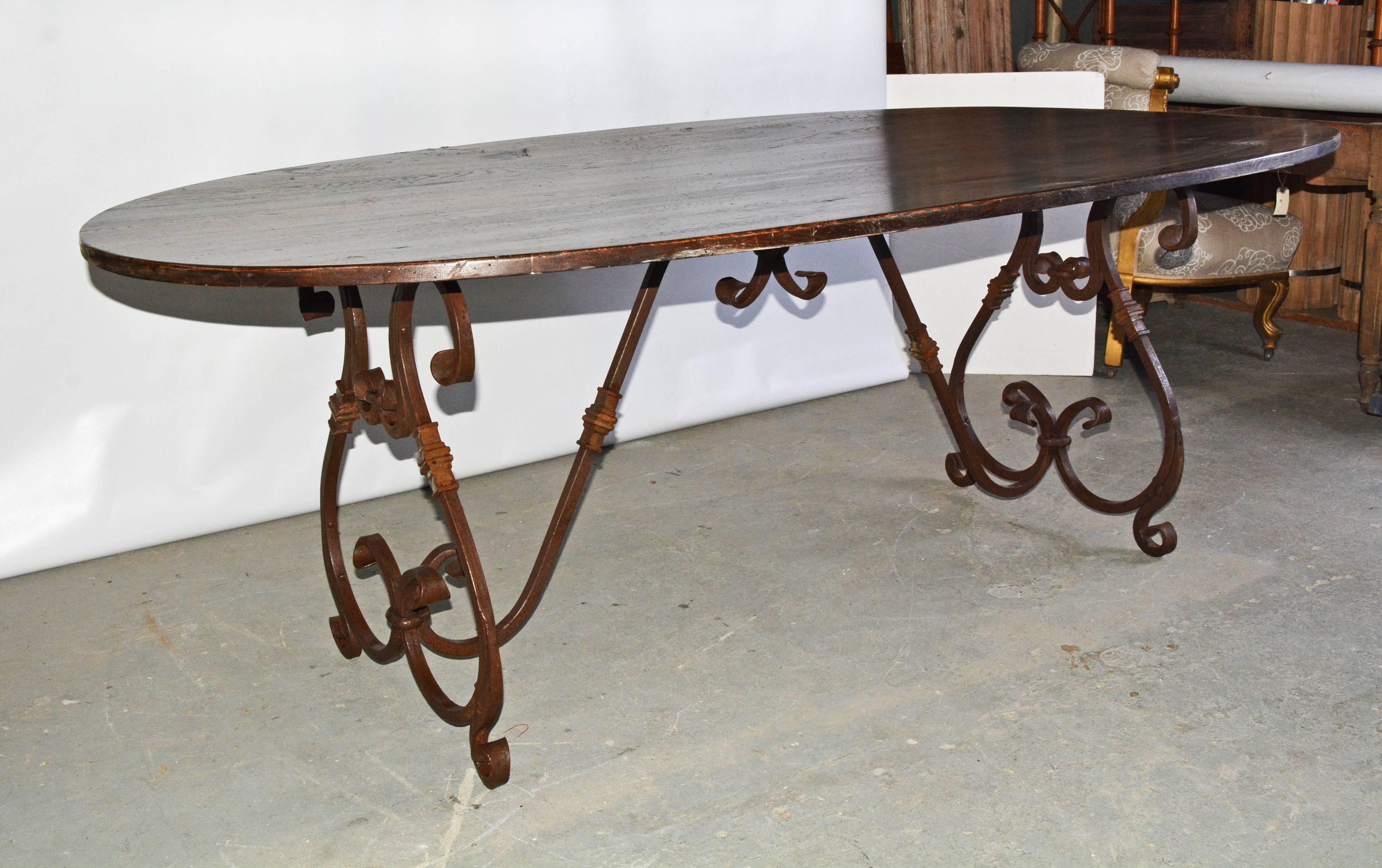 Elegant and rustic at the same time, the French Baroque style hand-forged iron trestle base features two lyre-shaped legs adorned with a weathered rust finish, connected to the underside of the top with a curved stretcher. The delicate volutes,