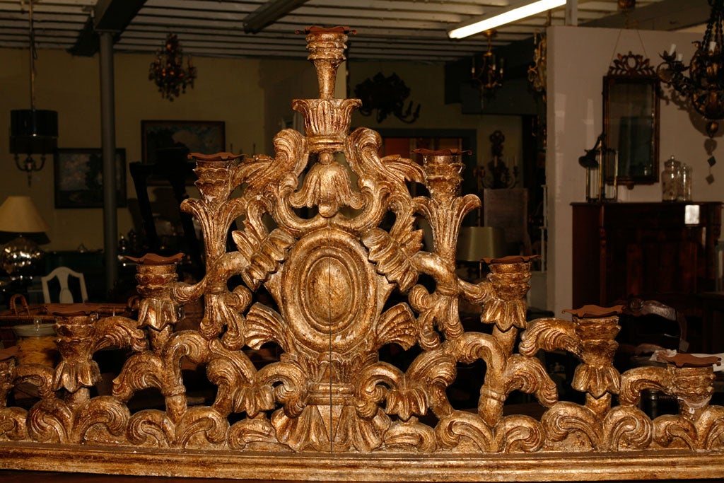 The antique Venetian pediment is made of hand-carved giltwood with a red undercoat. The elaborate carving is of equal rounded depth on both sides and could have topped a screen of some sort. The decorations include a centred bell flower, ovals,