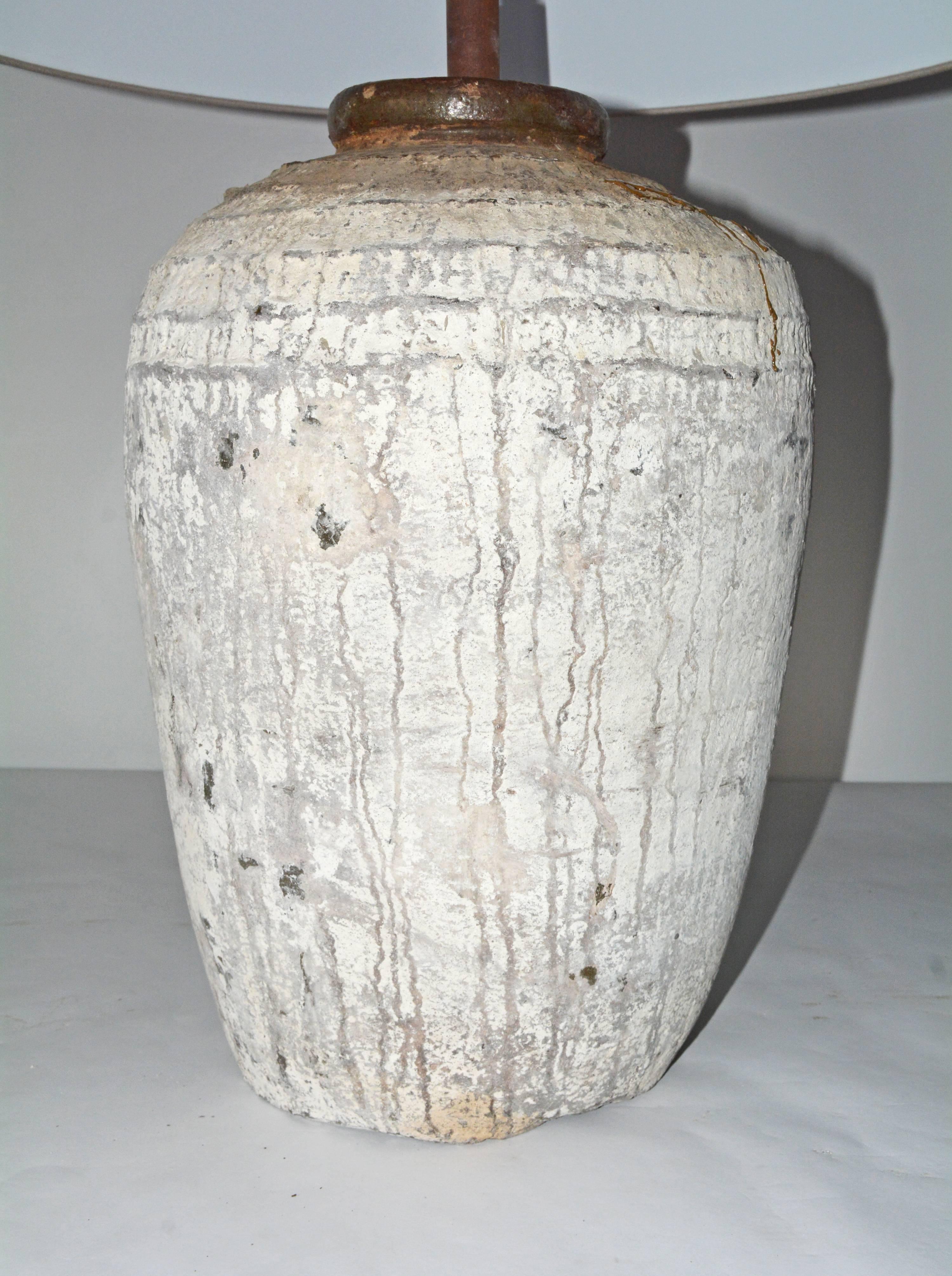 The large white/grey lamp base is a rustic antique Chinese clay jar. Chinese lettering is found at the bottom of one side. The shade is made of taupe cross-hatch Belgium linen. En relief bands circle the top of the jar. The lamp is wired for US