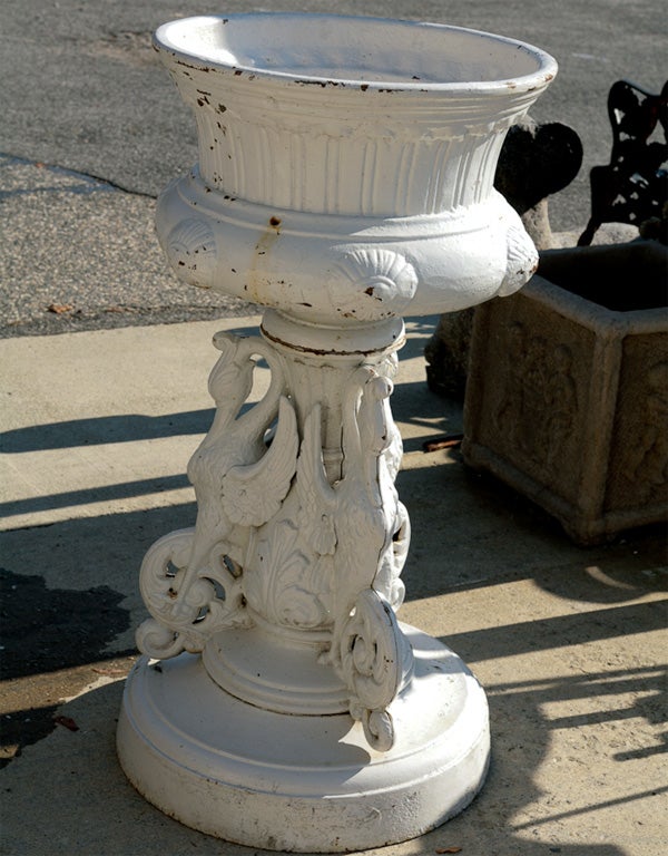 Pair of highly decorative Victorian cast iron urns consist of a round flared basin atop a pedestal embellished with three stylized winged swans, acanthus leaves and scrolls. The urns are painted white.