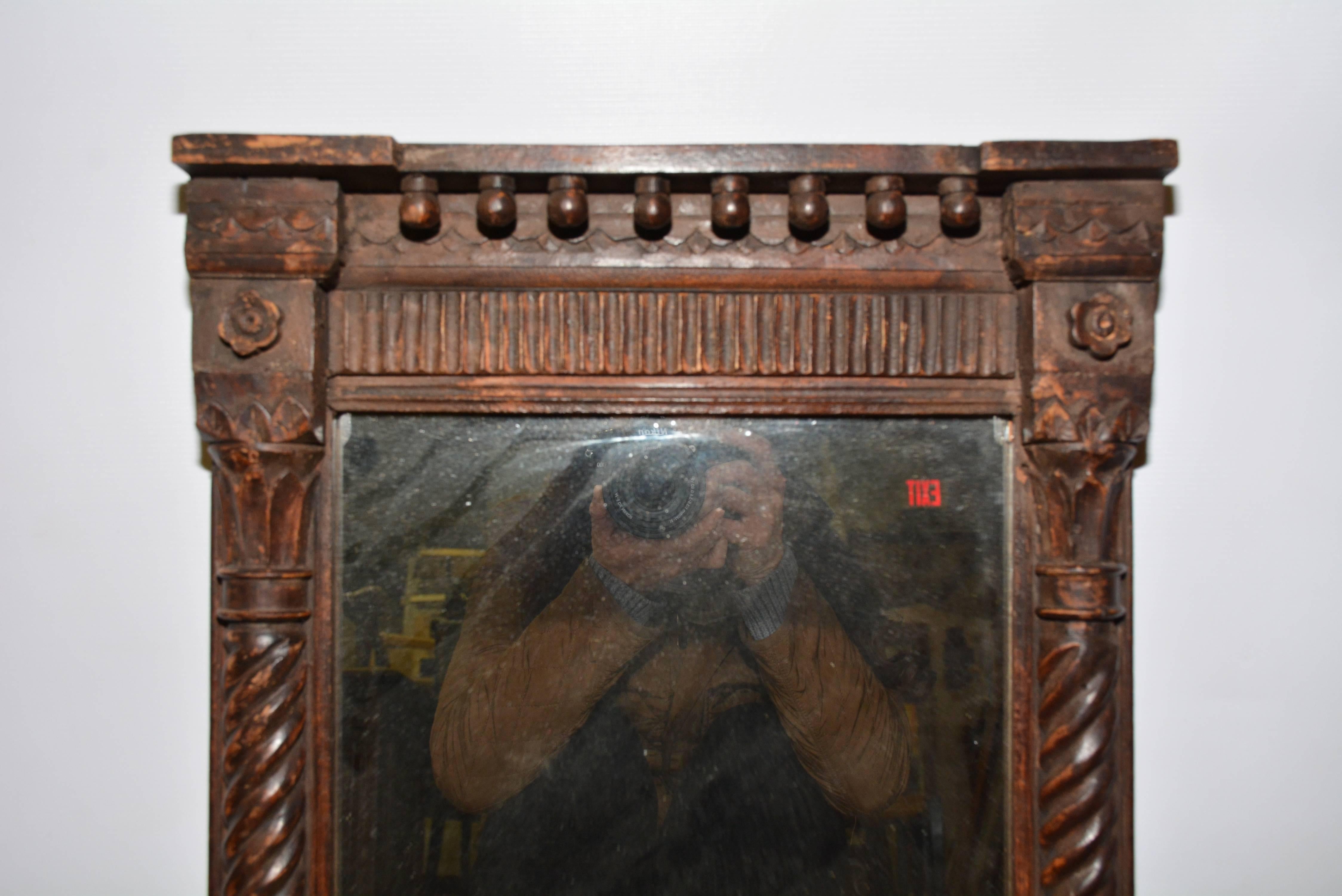 L'ancien miroir néoclassique sculpté à la main est en bois teinté et présente un sommet à capuchon avec une rangée de boules attachées et un panneau cannelé. Les côtés sont ornés de pilastres classiques tordus, de chapiteaux et de bases. Le fond est