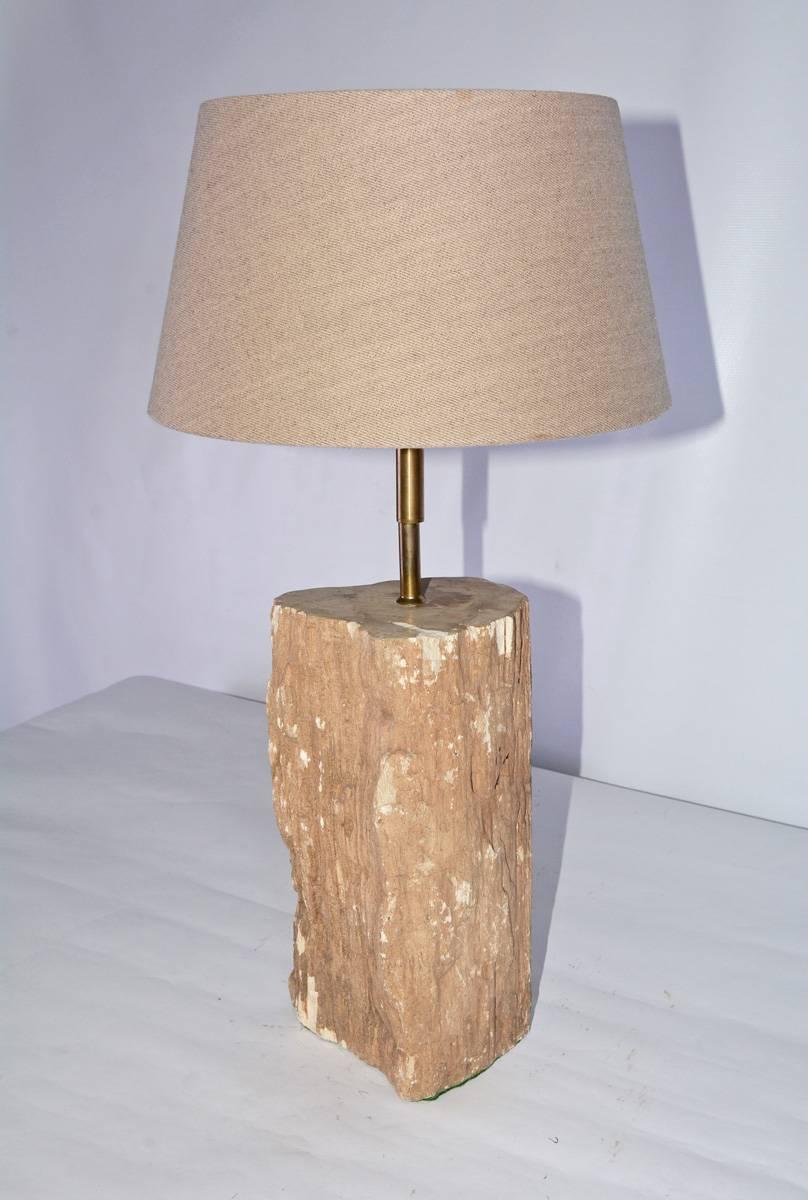 The contemporary lamp is made of a piece of light brown petrified wood and is electrified for US use. The switch is attached to the electric cord. The shade is of light brown Belgium linen with a plastic liner. The bottom is padded with green