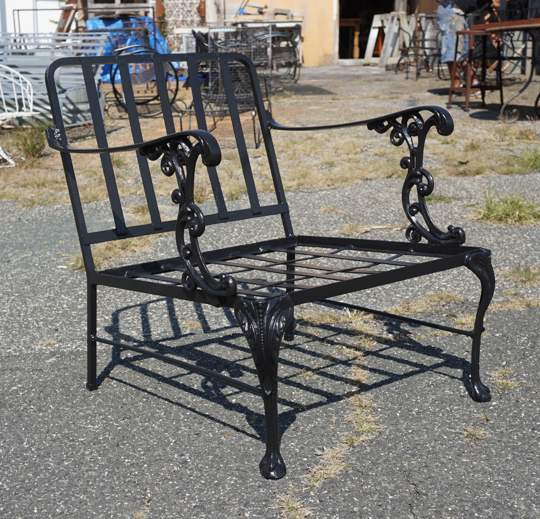 This set of three outdoor metal garden seating ensemble has generously wide, wrought iron chairs, arms decorated with Rococo supports, as well as cabriole legs. The matching two-tier table has similar features. Third matching chair with ottoman is