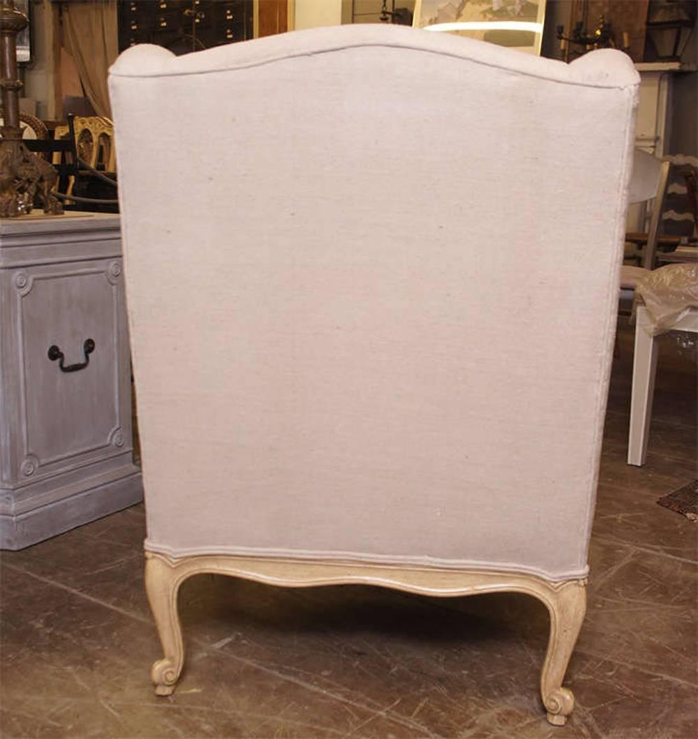 Louis XV provincial style wingback bergère in pickled oak, cabriole feet, undulating top crests; newly upholstered in linen.