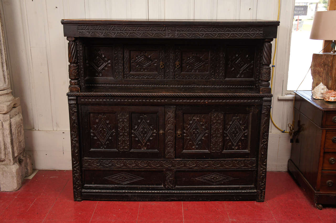 Elizabethan period, two-piece (top and bottom) antique Jacobean oak cabinet or cupboard with inset two-doors above and two-doors below, both running the full width of the piece. Hand-carved detailing throughout. Remanent of original paper lining the
