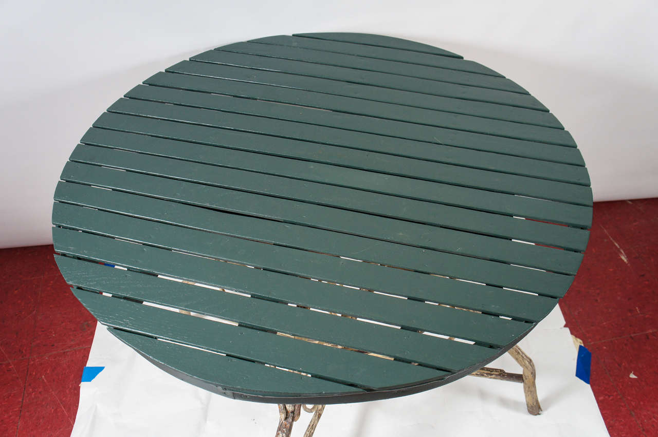 Rustic country round table is made of a bent twig base painted (peeling) paint and an openly spaced slated round top painted green. Great for the porch.