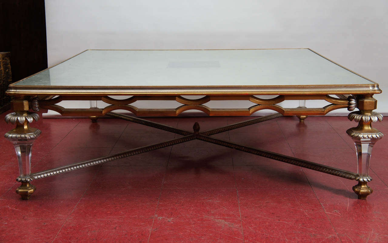 Making a major statement in size and detailing, this coffee table is composed of a glass top with an underlay of squares of silver leaf and set into a gold and silver frame. The top is supported by Baroque-style legs in gold, silver and clear custom