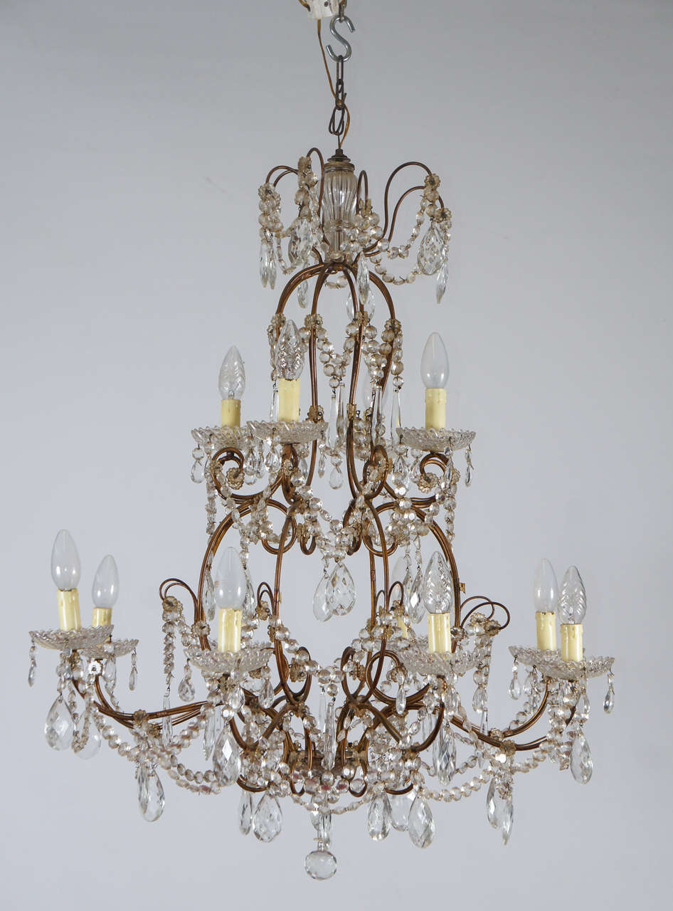 Designed with a gilt rococo scroll frame and hung with faceted beaded swags and faceted drops, this chandelier has twelve lights, eight below and four above, all with bobeches. Electrified for US use.