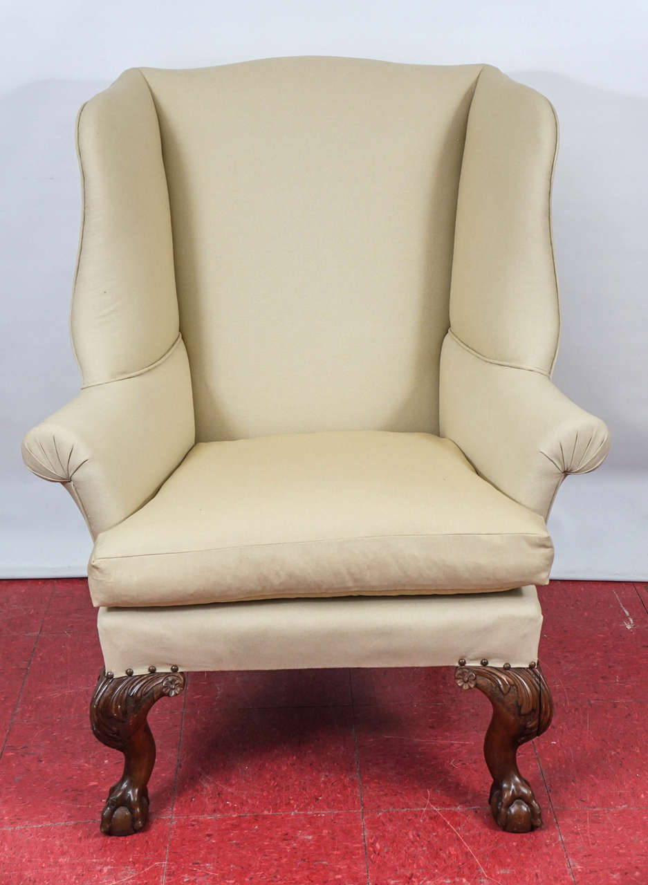 Substantial and comfortable wing chairs have carved cabriole ball-in-claw and leaf legs, separate cushions and are upholstered in beige fabric.

Measures: Arm height 25.75