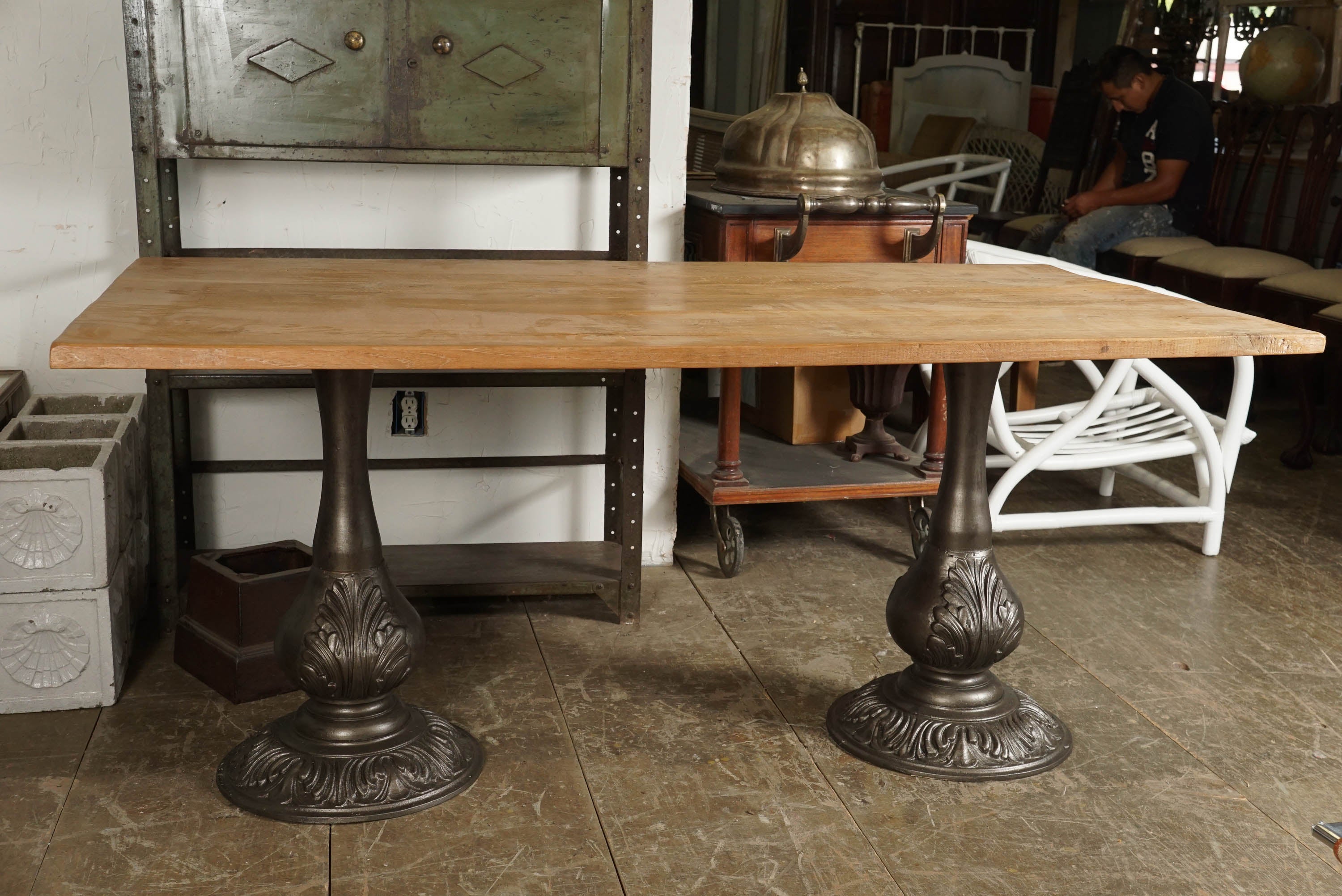 The top is composed of rustically smooth planks of teak wood, while the pair of pedestals are of antique silver cast iron. Each, decorated with acanthus leaves, has at the top four flanges with holes for securing the thick teak wood board. Top and