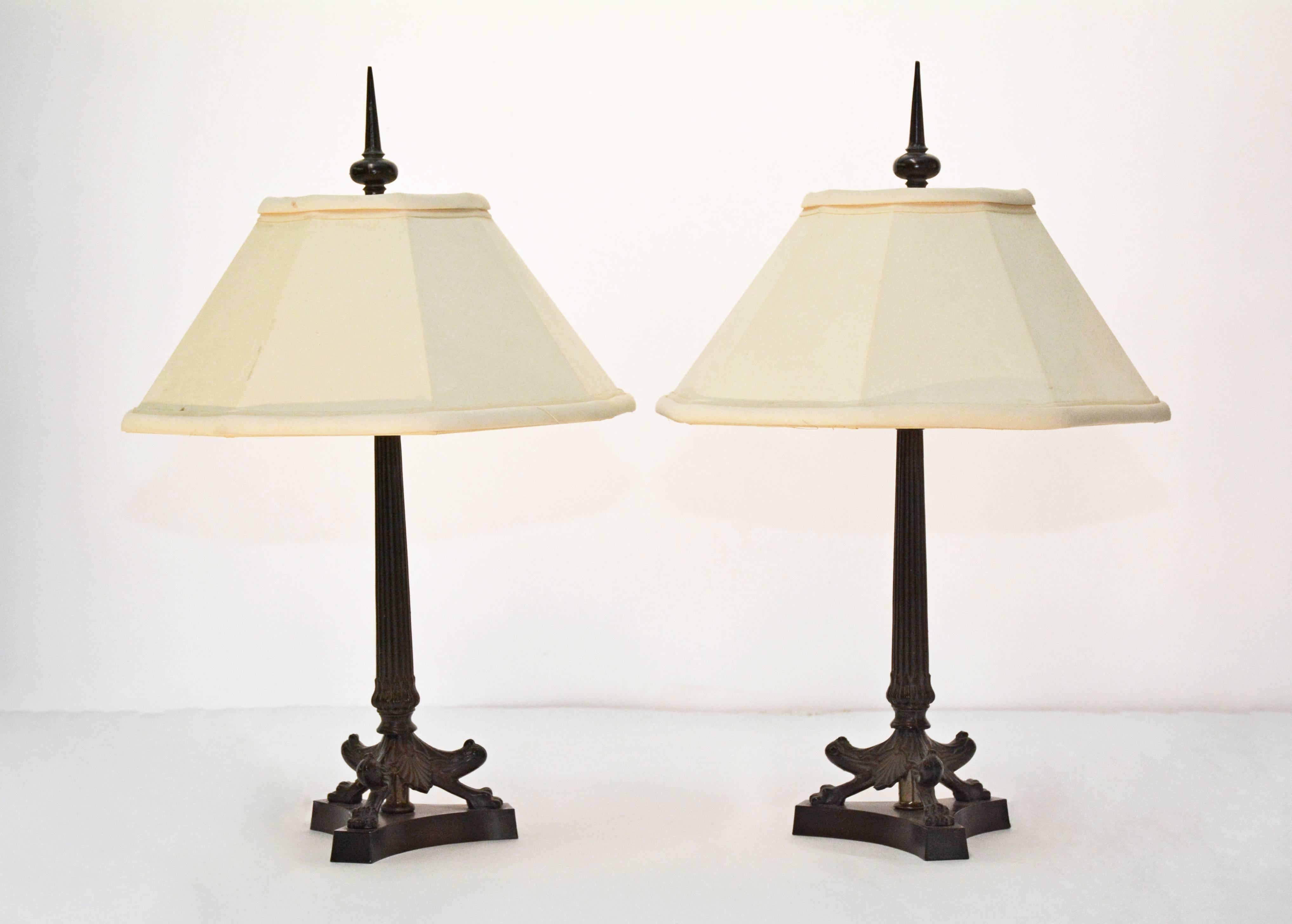 The pair of small classical Greco Roman-style lamps have column shafts set on three-legged and footed bases decorated with acanthus leaves and placed on platforms. The lamps are topped with bronzed spike finials. Each lamp, electrified for US use,