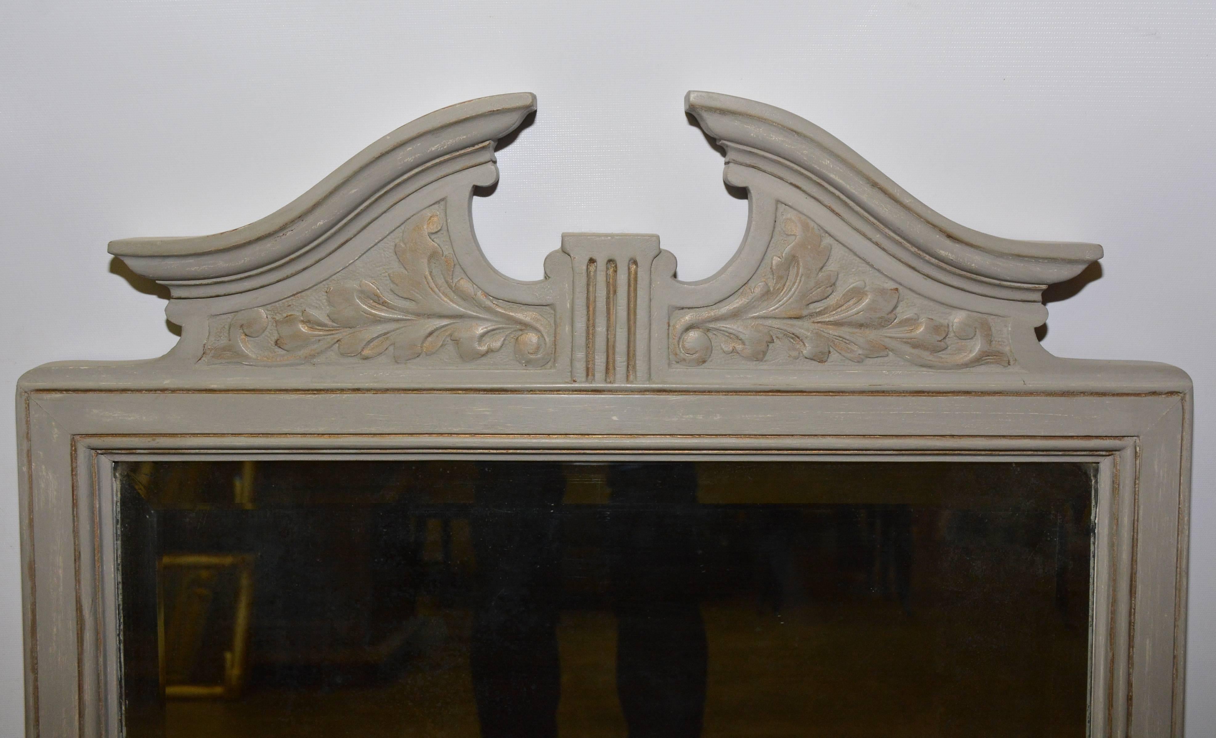 The square mirror frame is painted with a rubbed grey color and has a broken arch pediment decorated with leaves an relief. The silvered mirror is bevelled. The backing is wood and is wired for hanging. 
Use it for a fireplace mantel mirror, console