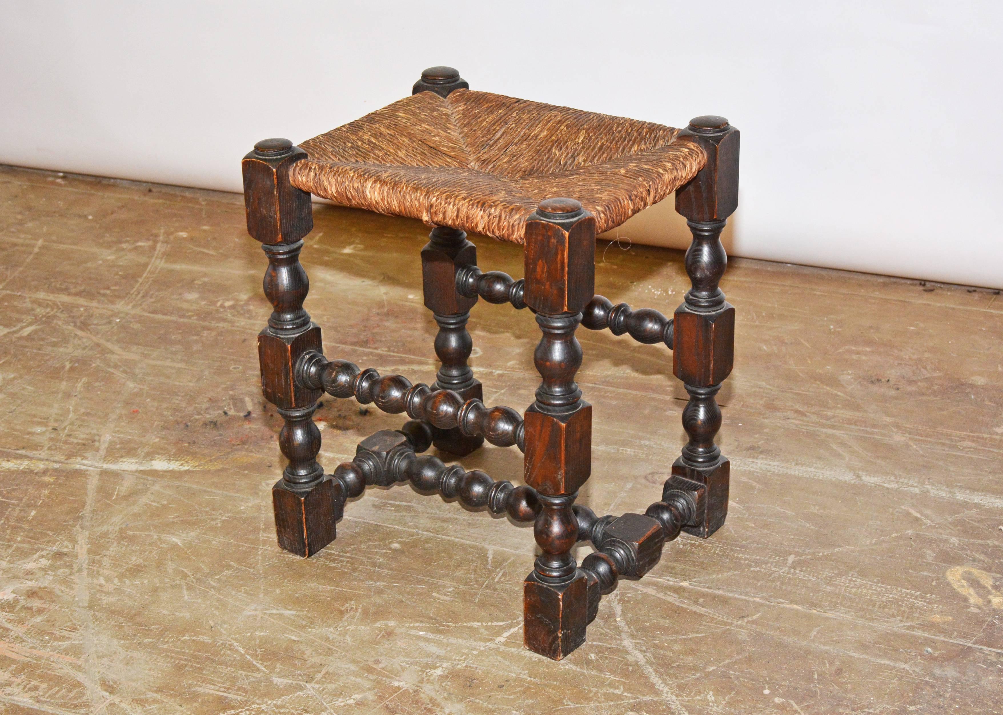 Der antike Hocker aus Hartholz mit einem Sitz aus Binsen hat kunstvoll gedrechselte Strecker und kühn gestaltete Beine.