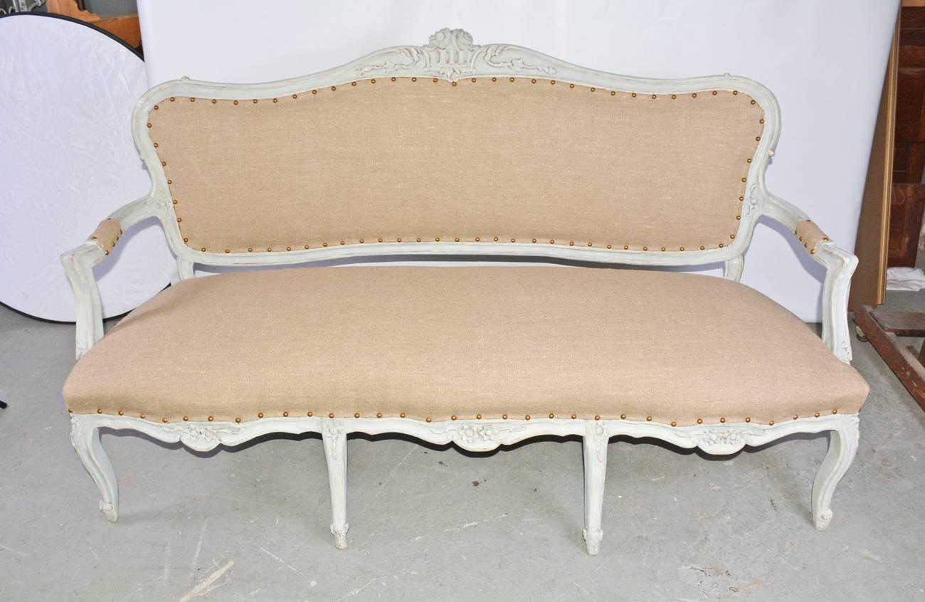 19th century French Louis XV style sofa or bench painted in a French blue-grey, with floral motives en relief. Newly reupholstered in a tan tight weave muslin.
Measures: Arm height 25
