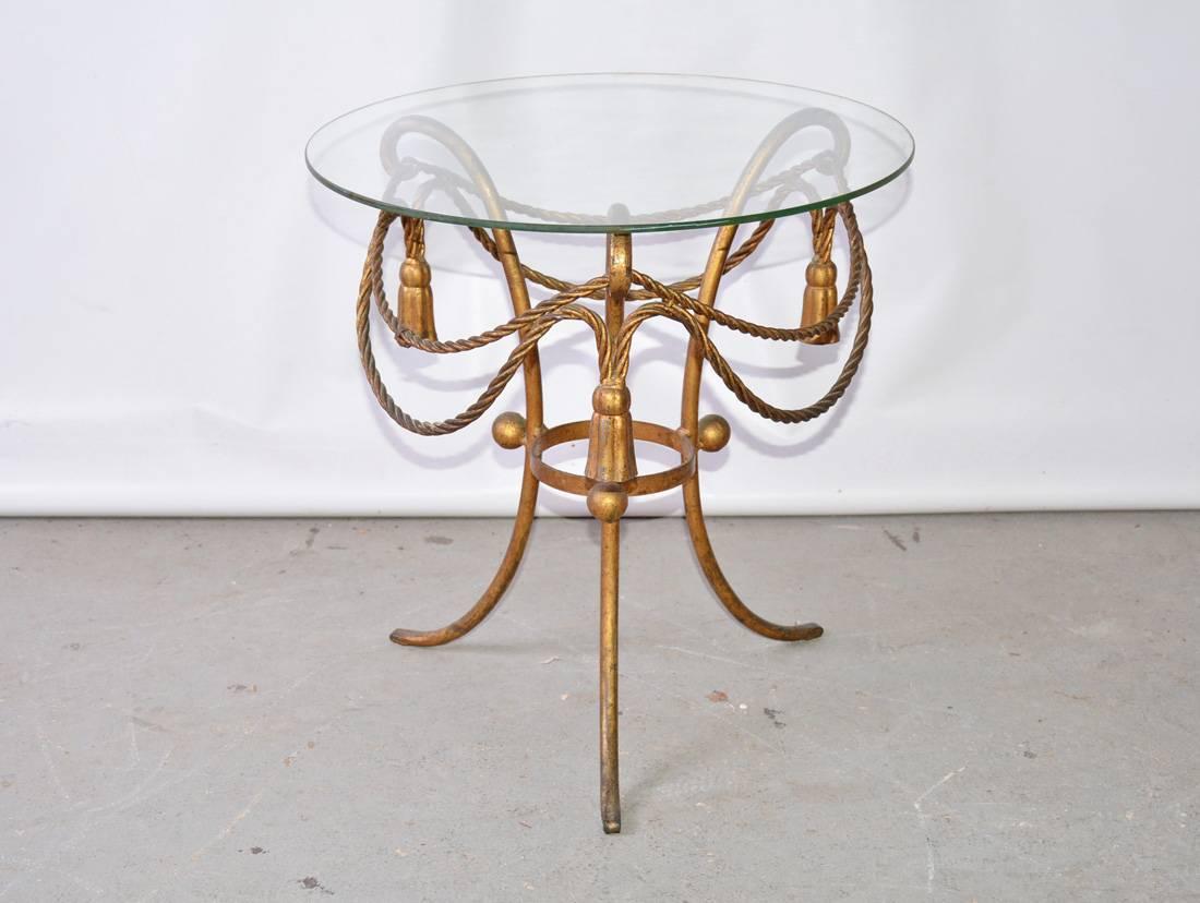 The vintage Italian lamp table is made of gilt-metal. Festooned with rope swags and tassels and has a round glass top. Great as occasional or side table. A larger piece of glass can be exchanged for the smaller removable glass top.