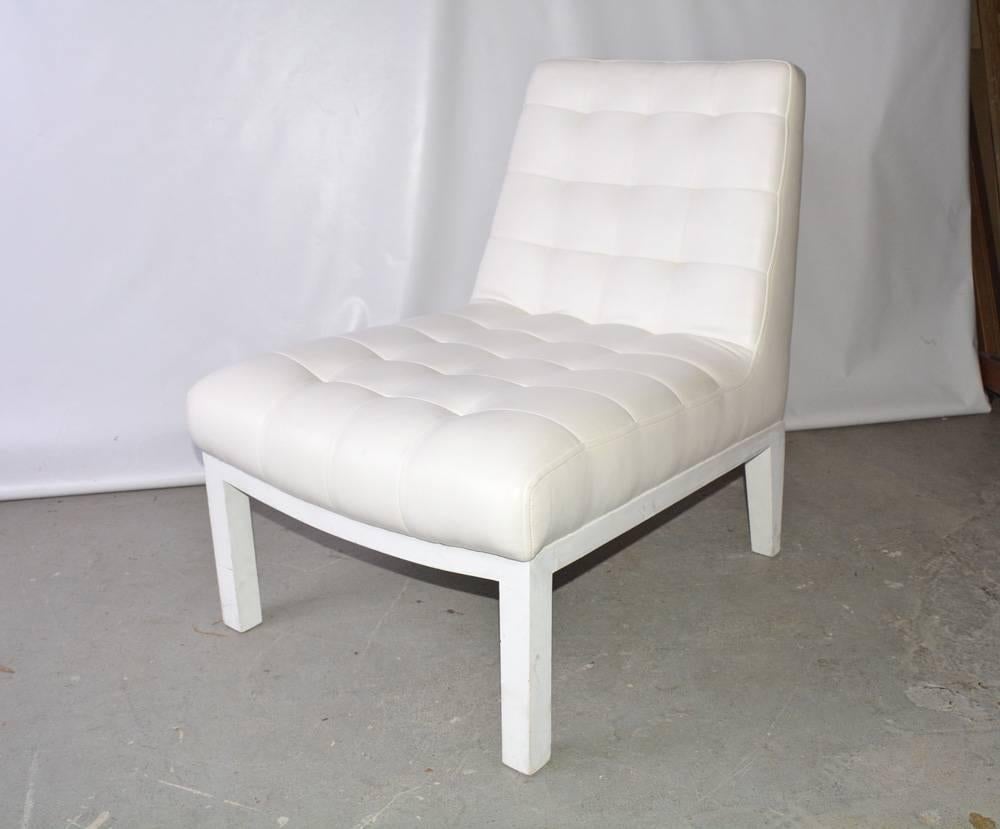 The contemporary slipper chair is upholstered in white tufted leather. The wood legs and frame are painted white.