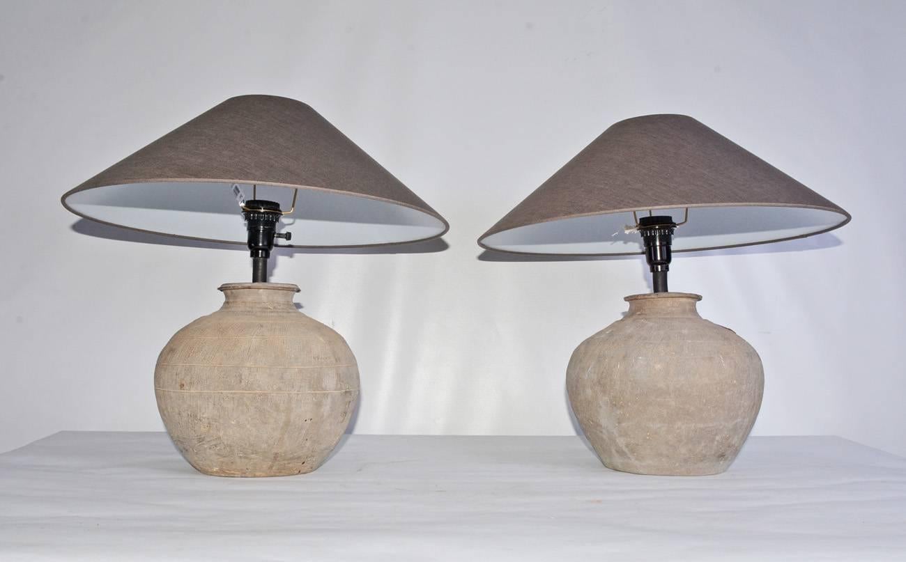 The pair of antique Chinese unglazed terracotta handcrafted belly jars are now lamps electrified for US use with Belgium linen shade.  Not an exact match since they are both hand made.
Bulb socket are euro type so will require euro shades or socket