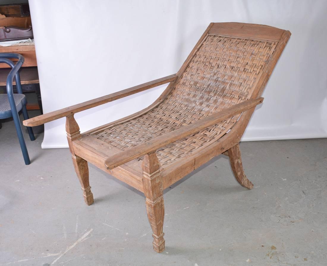 Chaise de plantation ou de planteur en teck de l'époque coloniale britannique, pour l'intérieur ou l'extérieur, avec assise et dossier en rotin. Merveilleuse patine du bois usé par les intempéries. 

